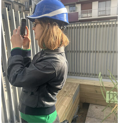 Photo d'une collaboratrice de l’agence là-haut avec un casque de protection bleu en train de prendre une photo sur un chantier