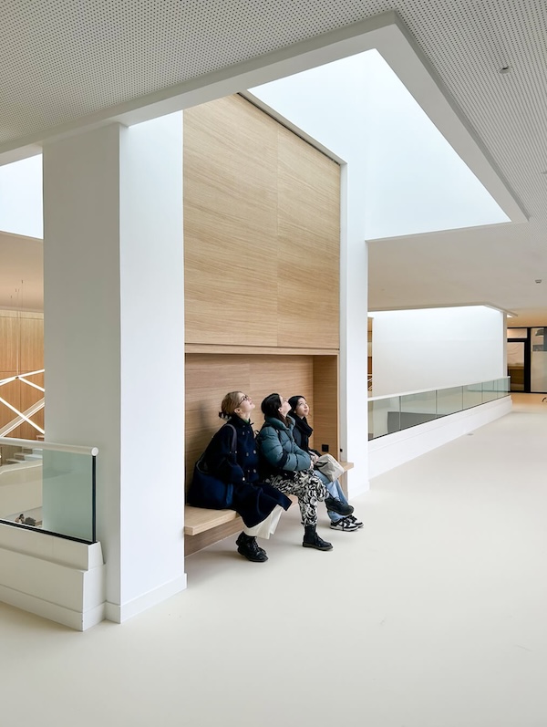 Trois femmes assises sur un banc du hall de l'Essec après le projet de restructuraton et extension agence là-haut