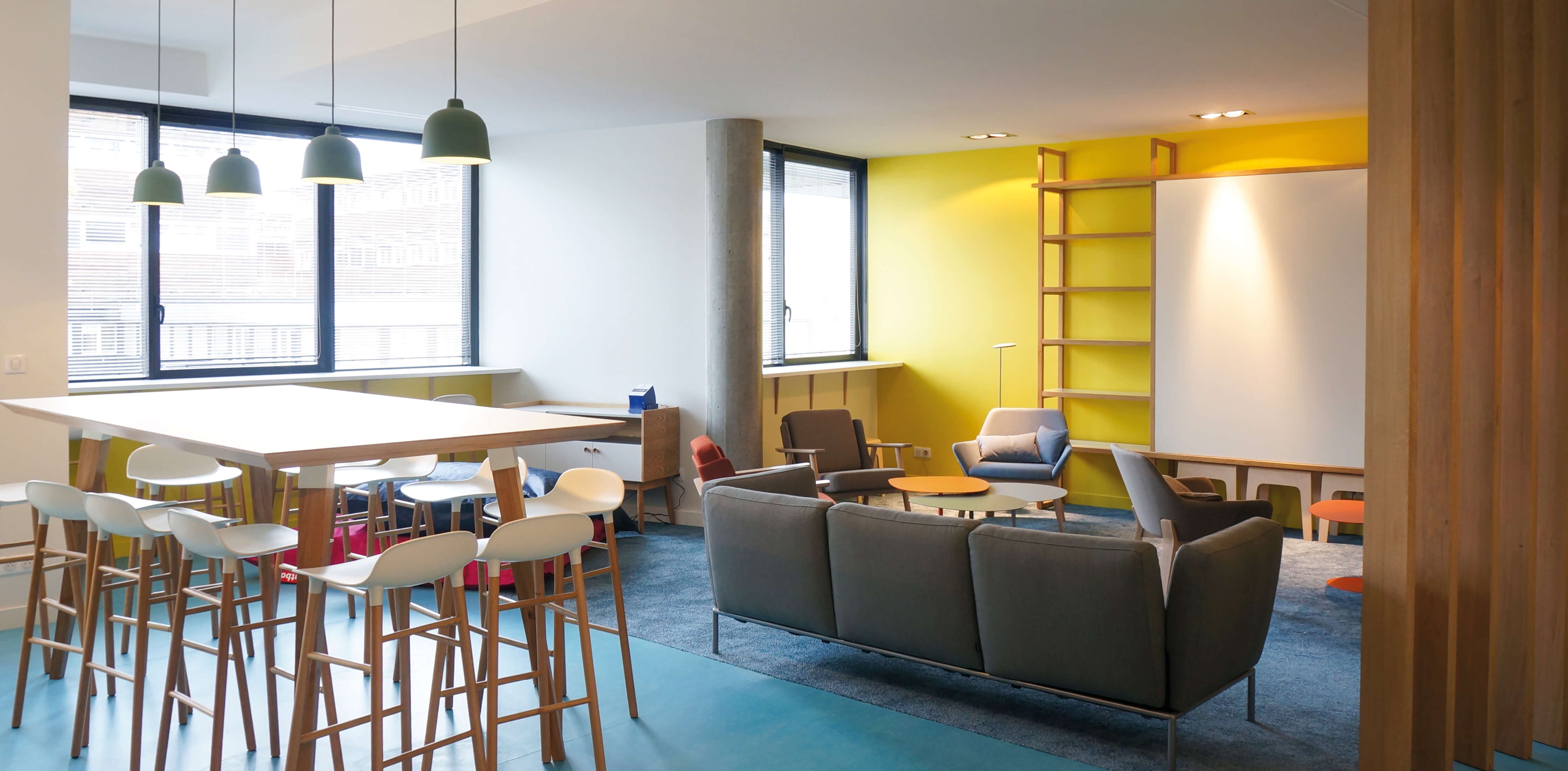 Photo de la salle des professeurs de l’Essec montrant l’espace détente avec le mur jaune en fond et la table haute sur mesure pour les échanges conviviaux