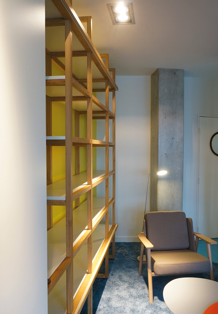 Photo en gros plan de la bibliothèque modulable installée sur un mur jaune dans la salle des professeurs de l’Essec