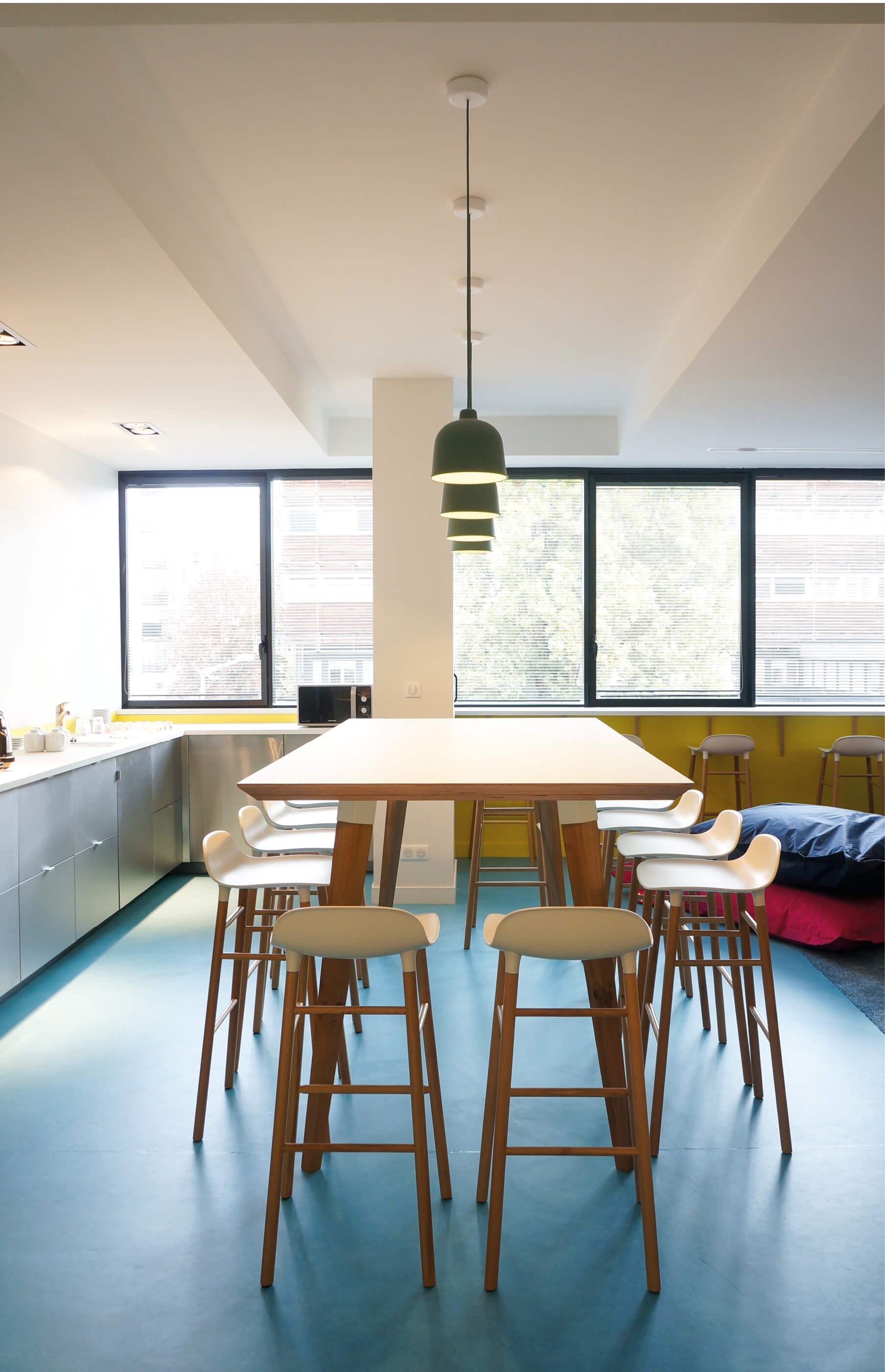 Photo montrant la table haute sur mesure de la salle des professeurs de l’Essec, une partie du coin cuisine et la lumière entrant par les fenêtres qui donnent sur le campus.