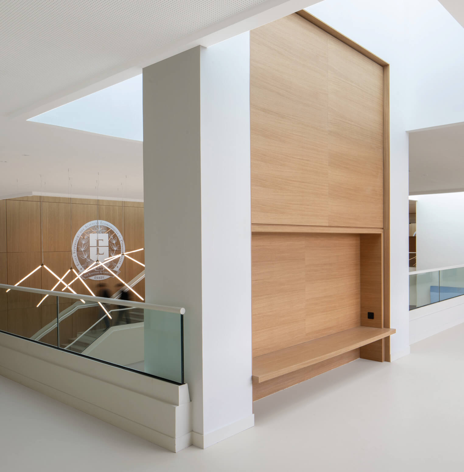 Photo du premier étage du grand hall de l'Essec après la restructuration campus qui laisse voir un intérieur lumineux avec alcôve abritant une banquette en bois et un grand escalier.
