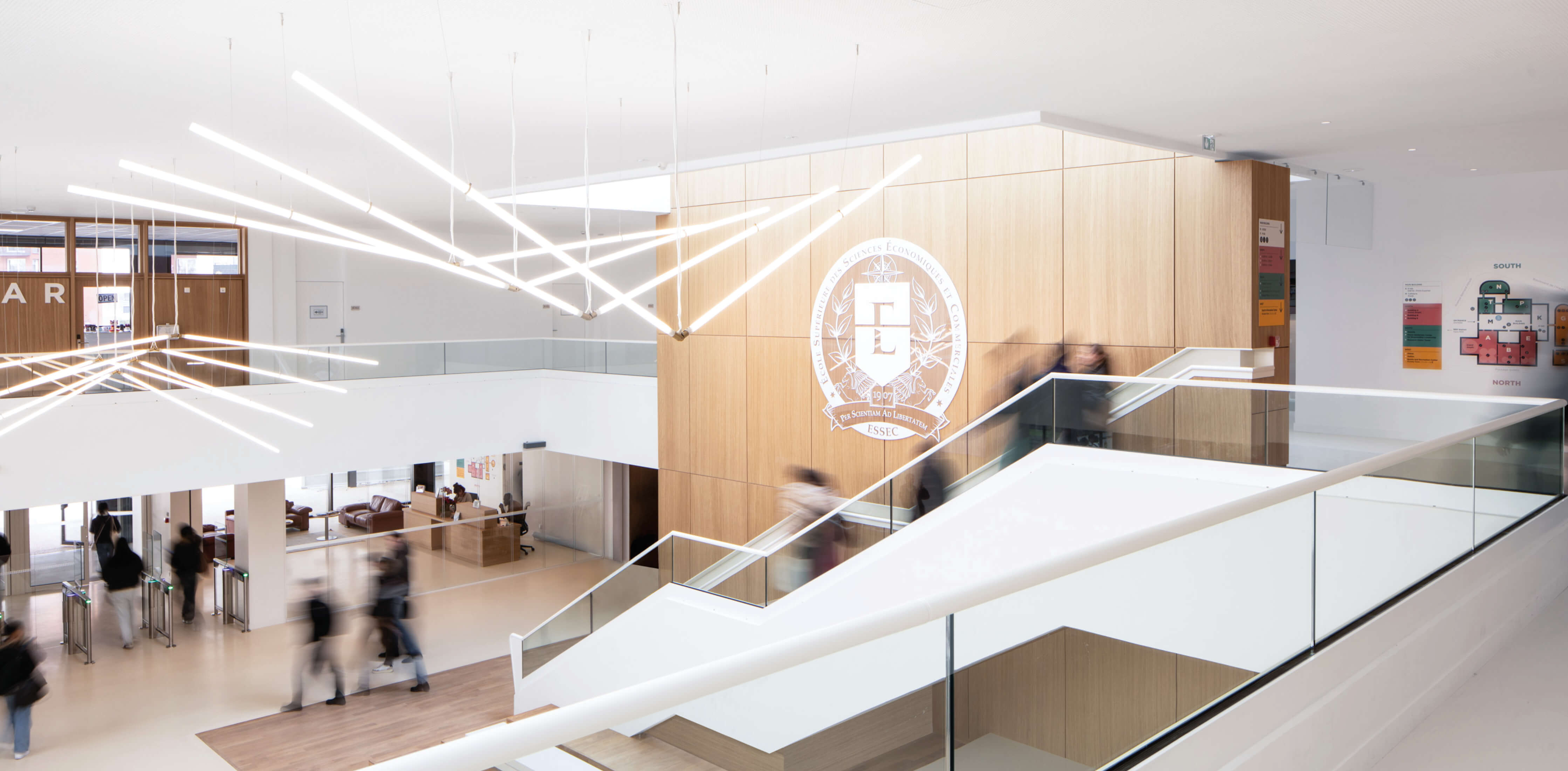 Photo du grand hall lumineux de l'Essec prise du premier étage avec des silhouettes d'étudiant en mouvemenet après les travaux de restructuration campus.