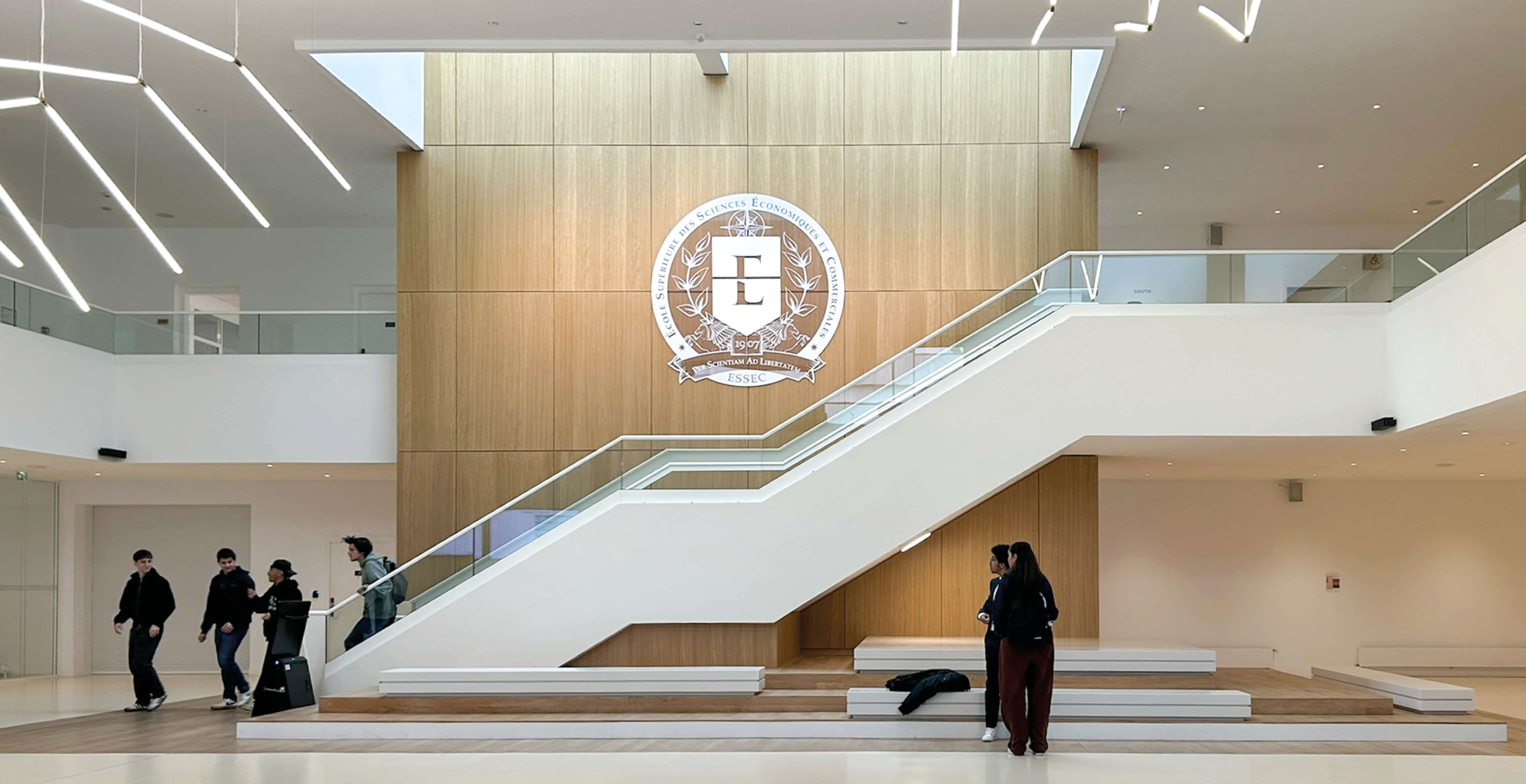 Photo latérale du grand escalier du hall de l'Essec, blanc et bois, après le projet de restructuration campus.