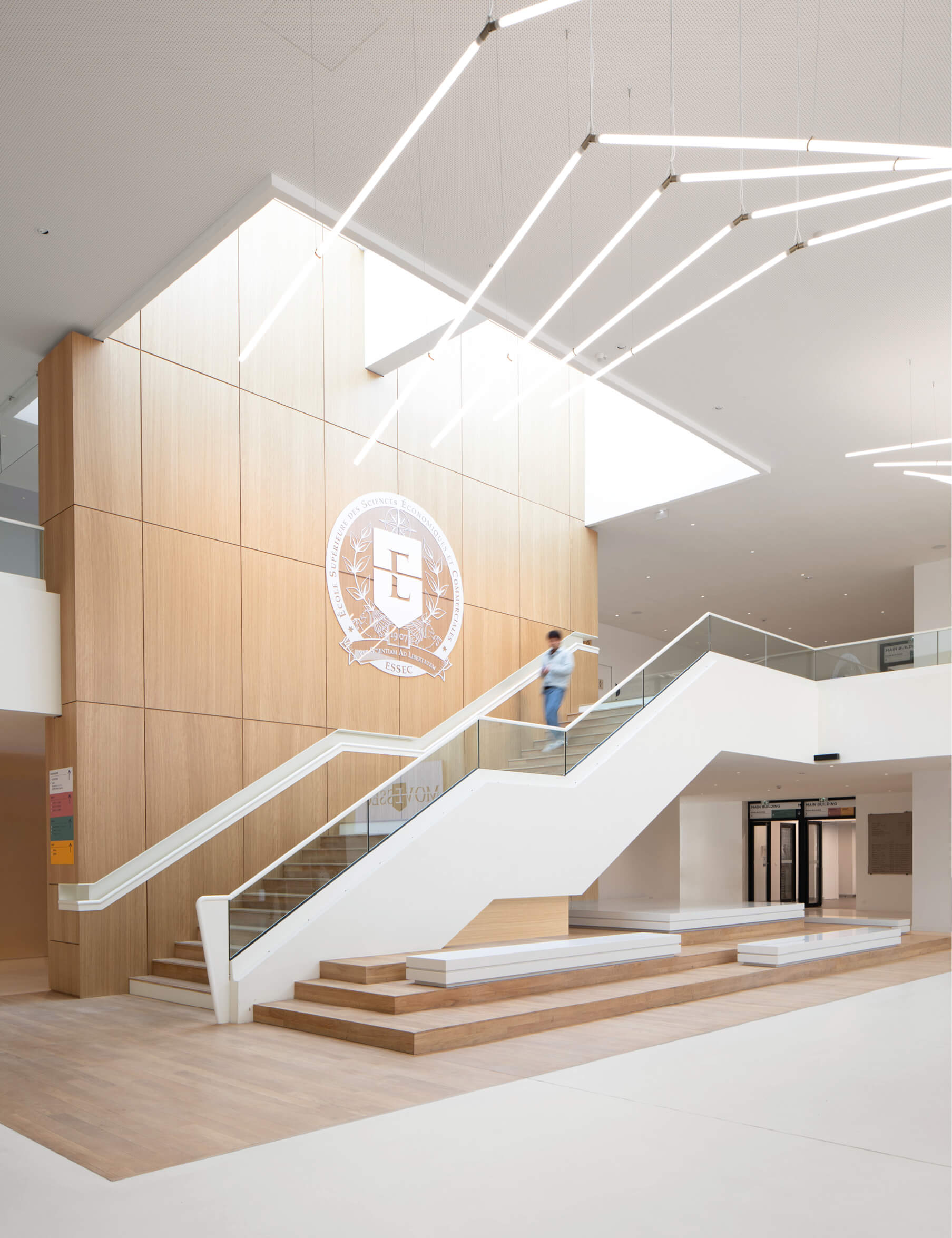 Photo montrant l'escalier, les gradins et le lustre du grand hall lumineux de l'Essec Cergy après restructuration du campus.