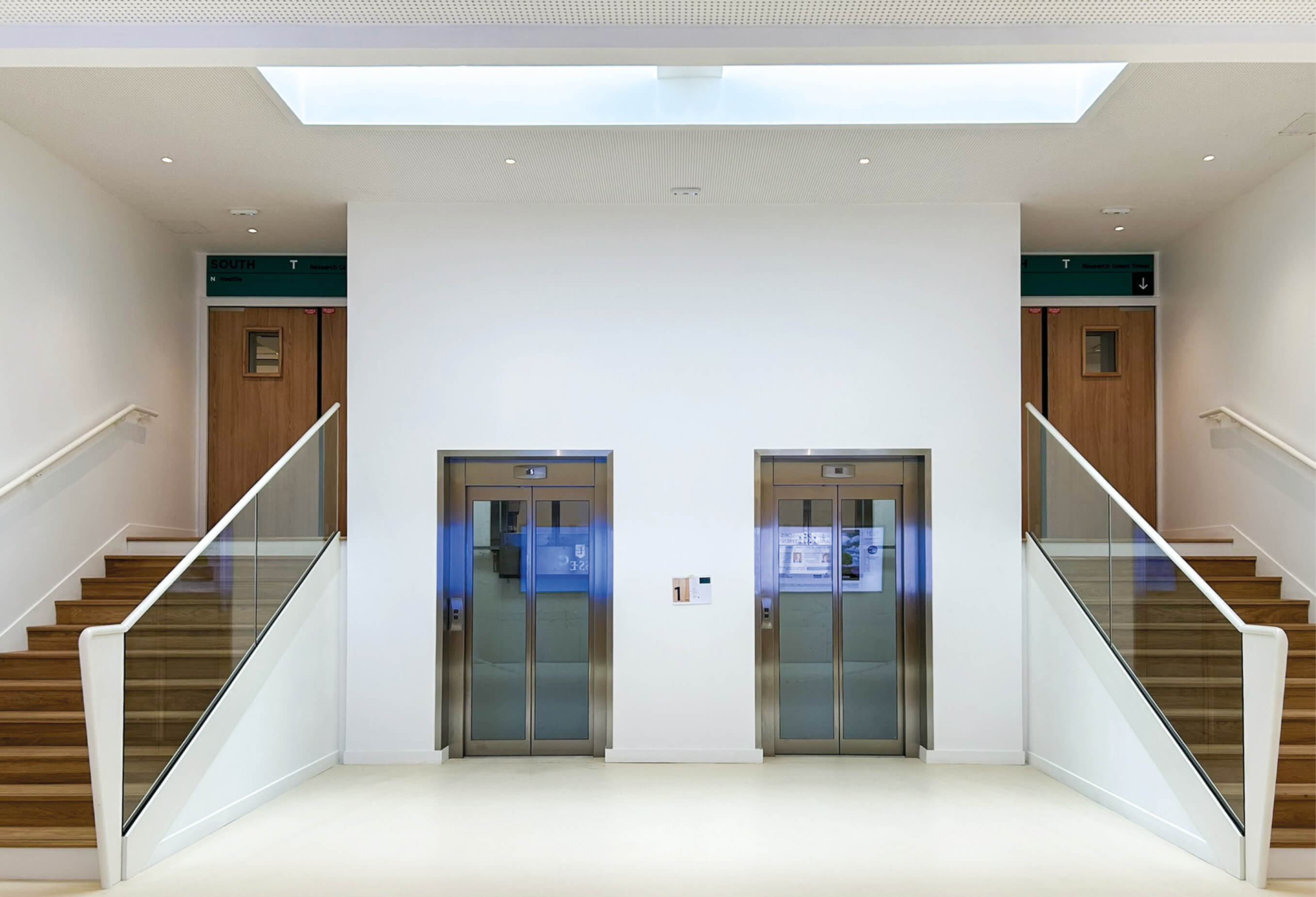 Photo de deux ascenseurs encadrés de deux escaliers conduisant à des portes battantes amenant à la Research Green Tower.