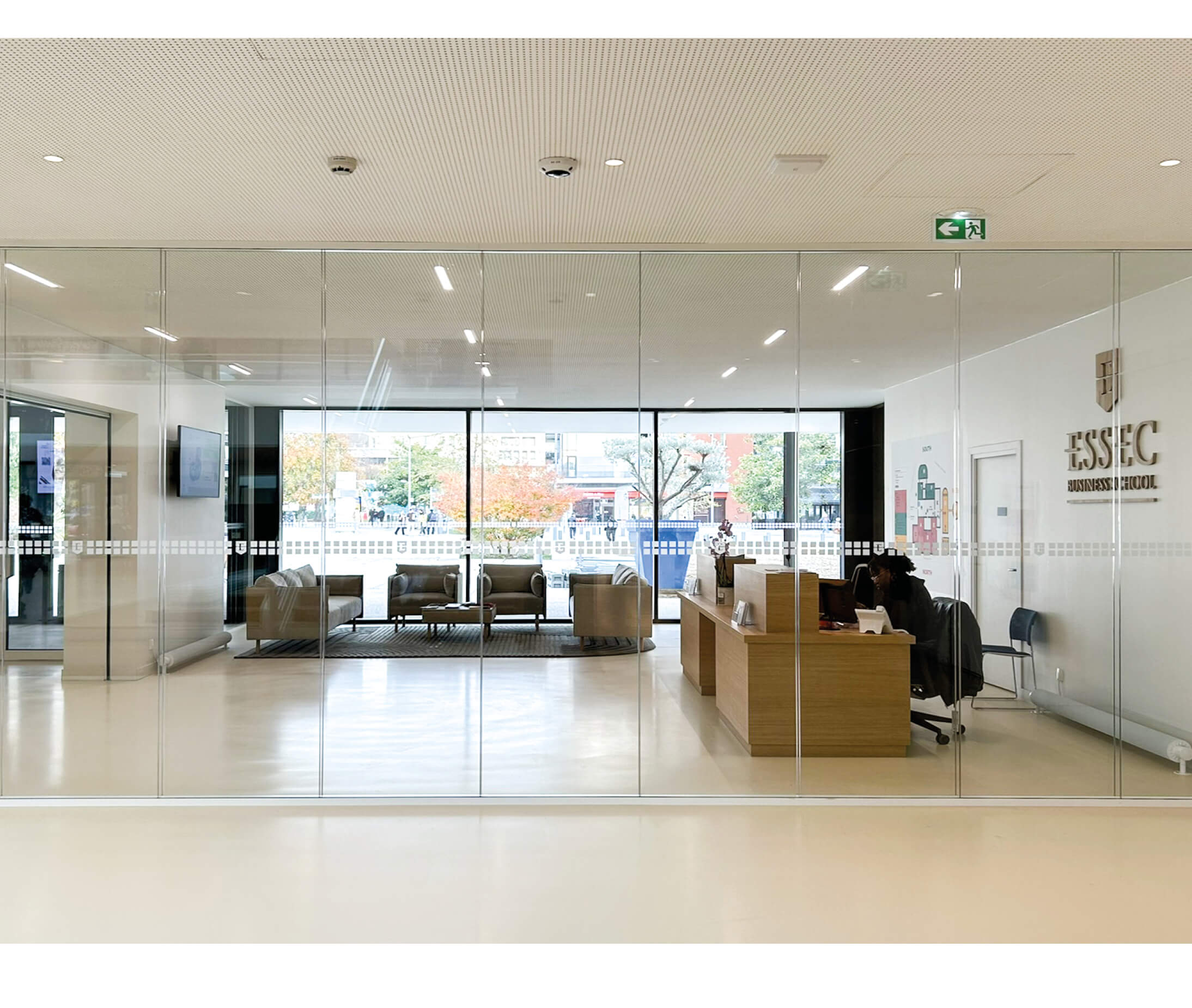 Photo d'un bureau et d'un espace d'accueil lumineux, derrière une baie vitrée, après la restructuration du campus de l'Essec Cergy.