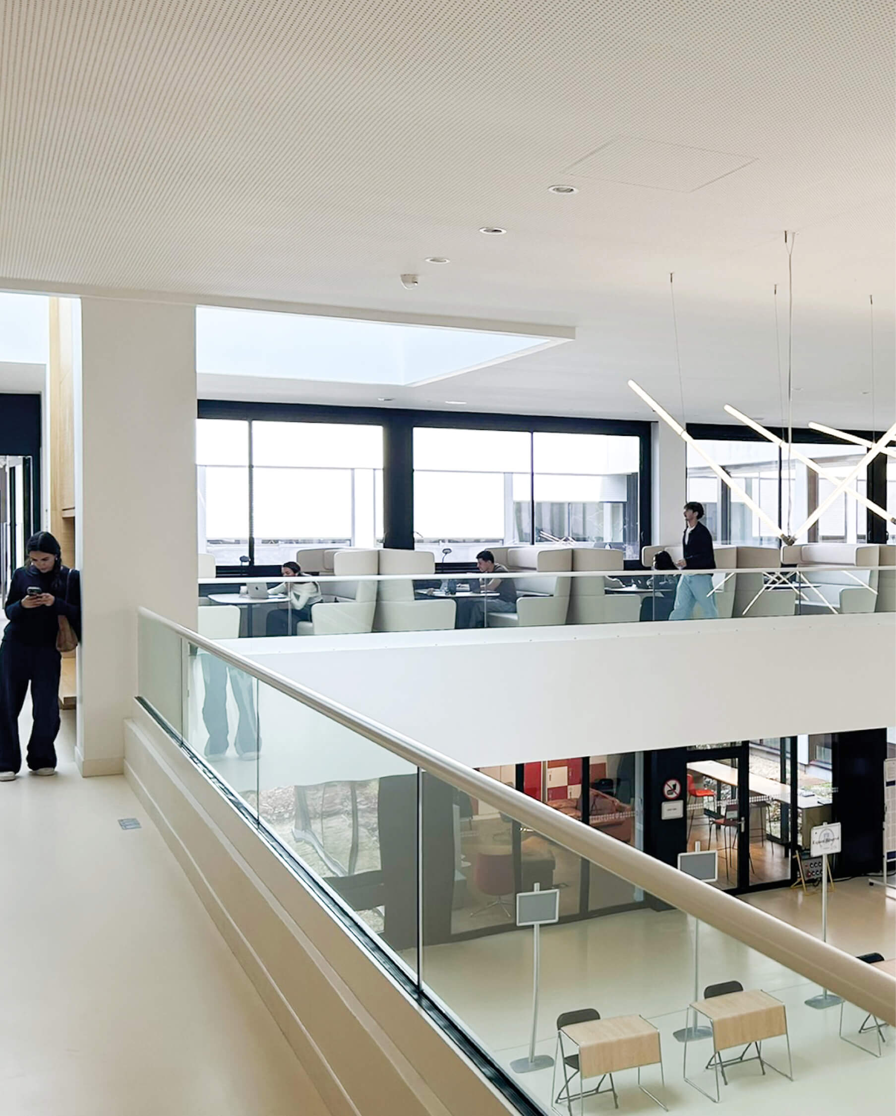 Photo d'ambiance du premier étage du grand hall de l'essec avec des élèves installés dans de grands fauteuils pour travailler, une autre consultant son téléphone près de l'alcôve.