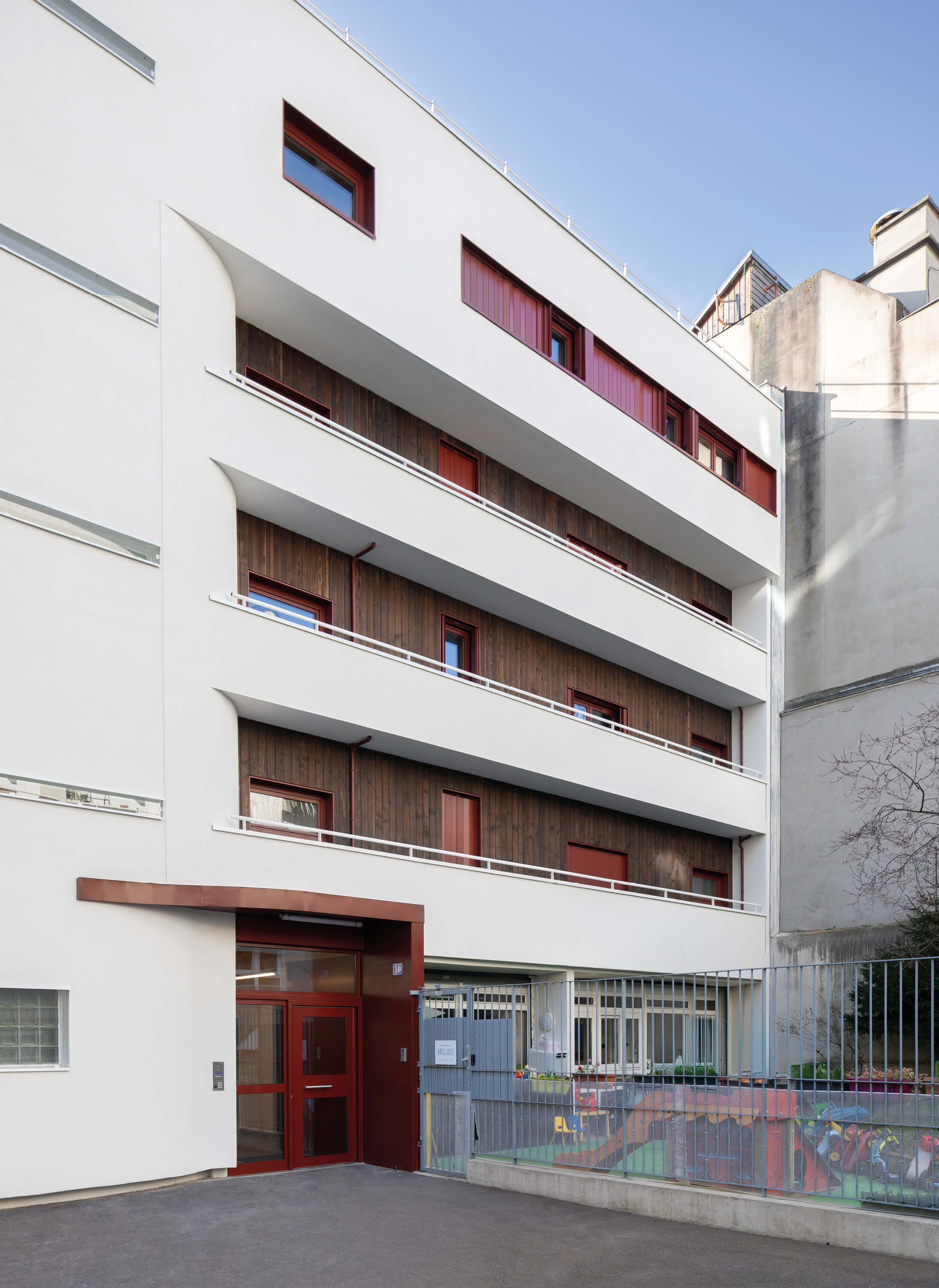 Photo de la façade nord mêlant le blanc, le bois et des touches de rouge après réhabilitation énergétique en milieu habité Impasse Delépine à Paris.