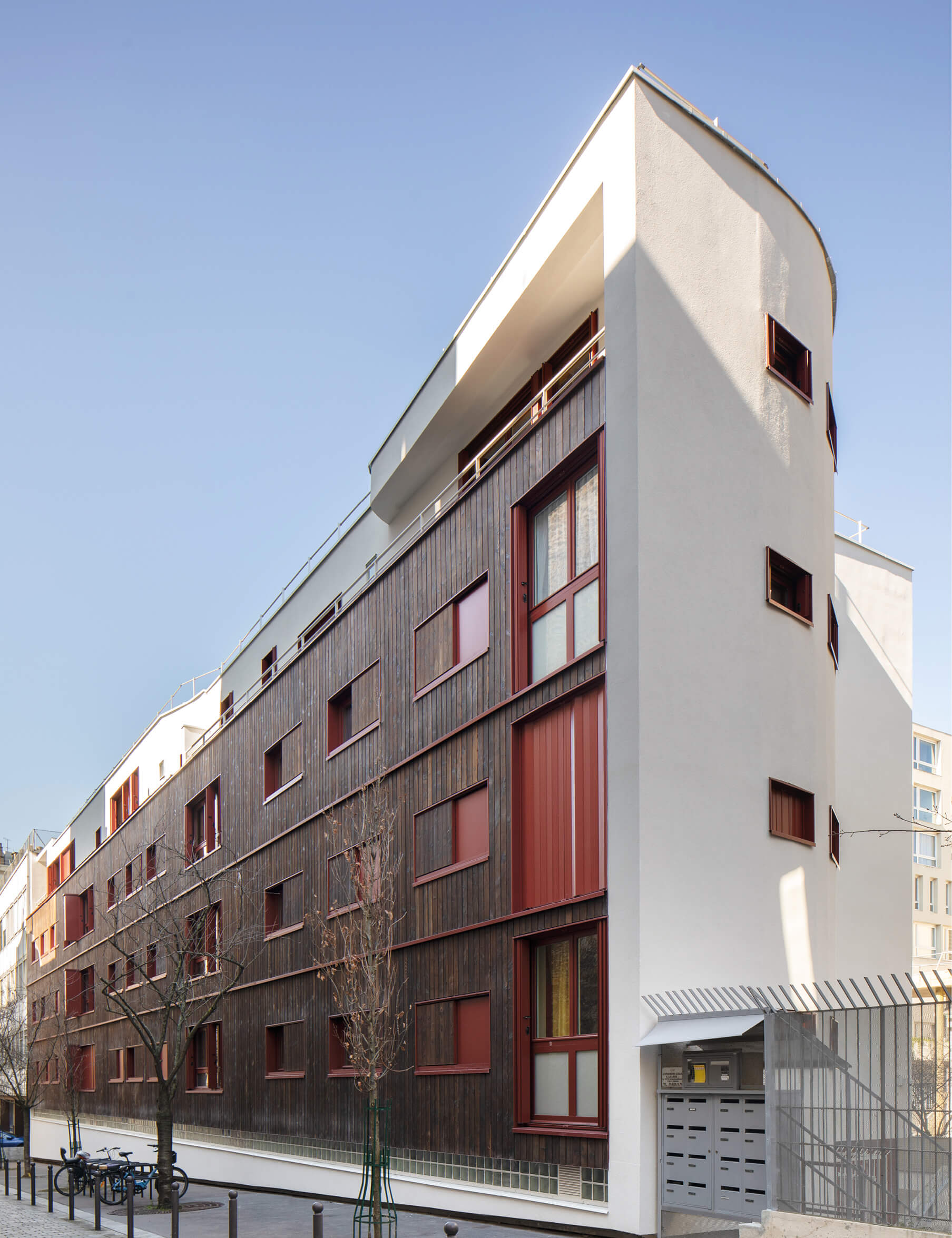 Photo de la façade sud mêlant le blanc, le bois et des touches de rouge après réhabilitation énergétique en milieu habité Impasse Delépine à Paris.