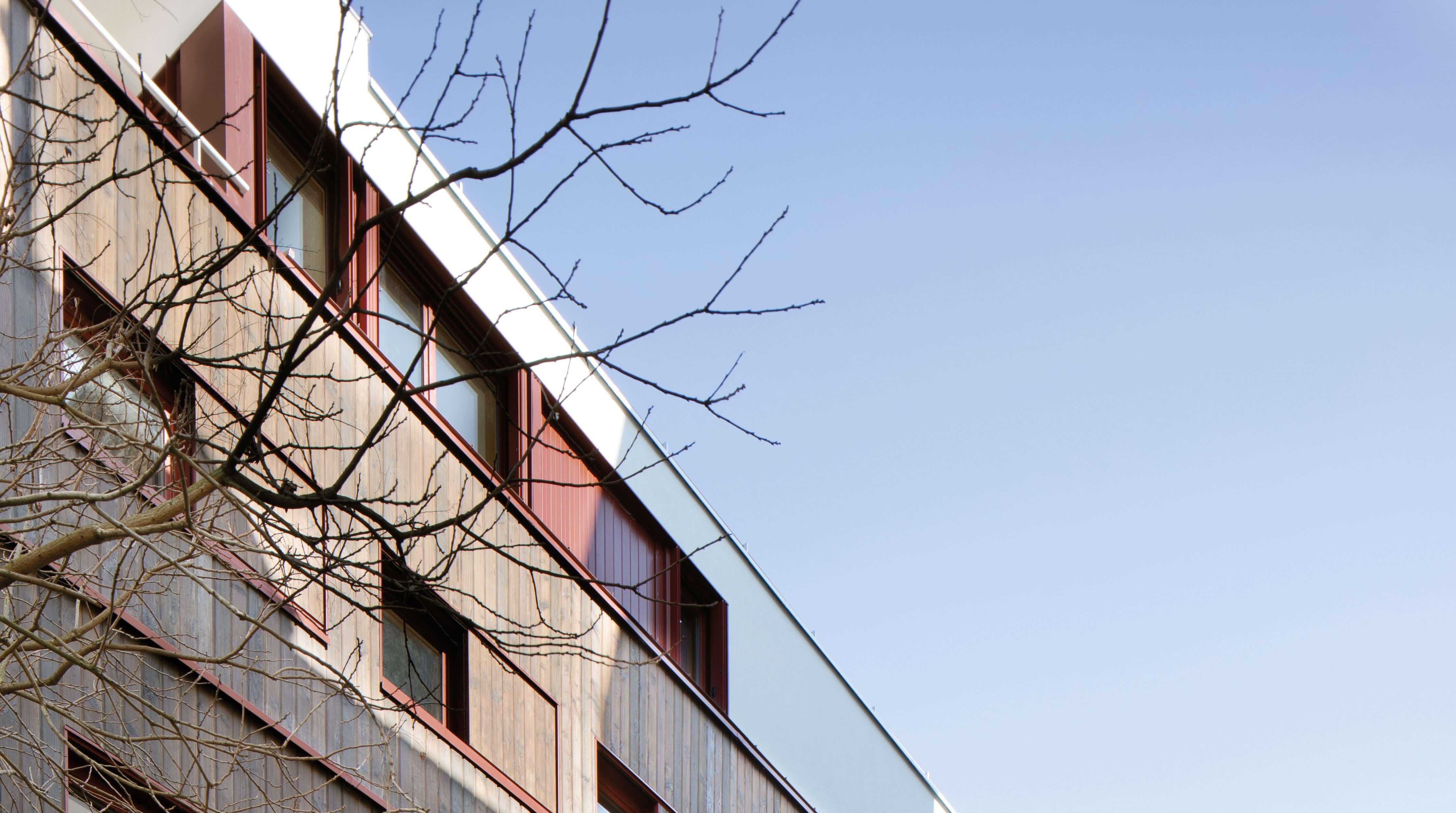 Photo sous un ciel bleu montrant la nouvelle façade sud blanche, bois et rouge de l'immeuble impasse Delépine après réhabilitation énergétique.