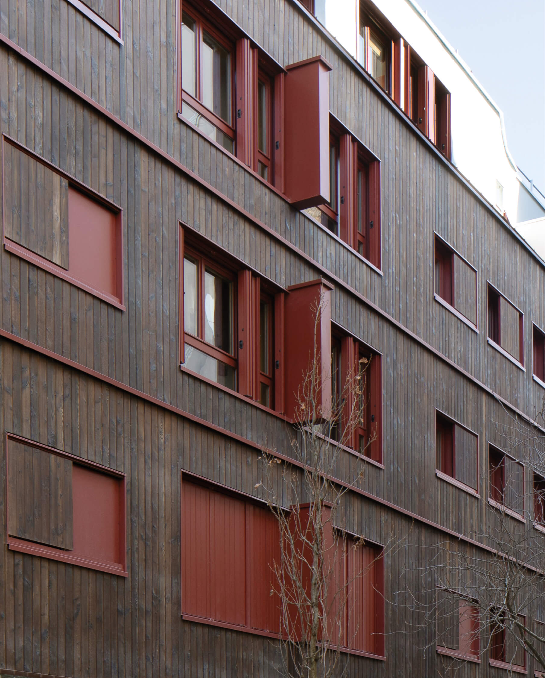 Photo sous un ciel bleu montrant la nouvelle façade sud blanche, bois et rouge de l'immeuble impasse Delépine après réhabilitation énergétique.