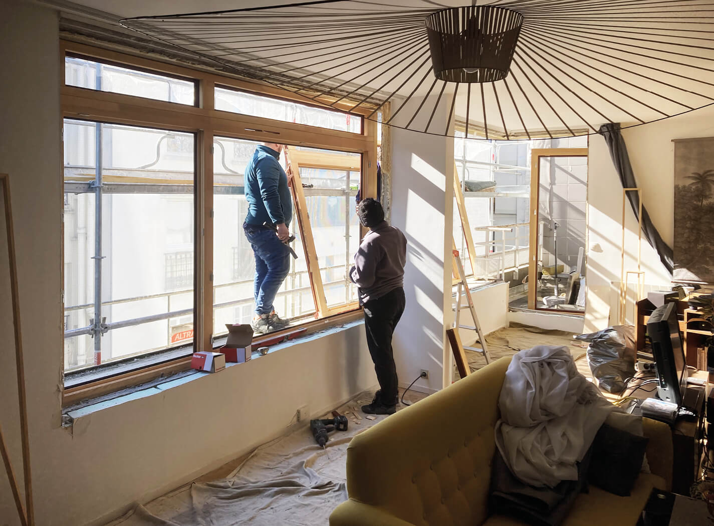 Photo prise pendant le chantier de réhabilitation énergétique en milieu habité de deux ouvriers en train de poser une menuiserie.