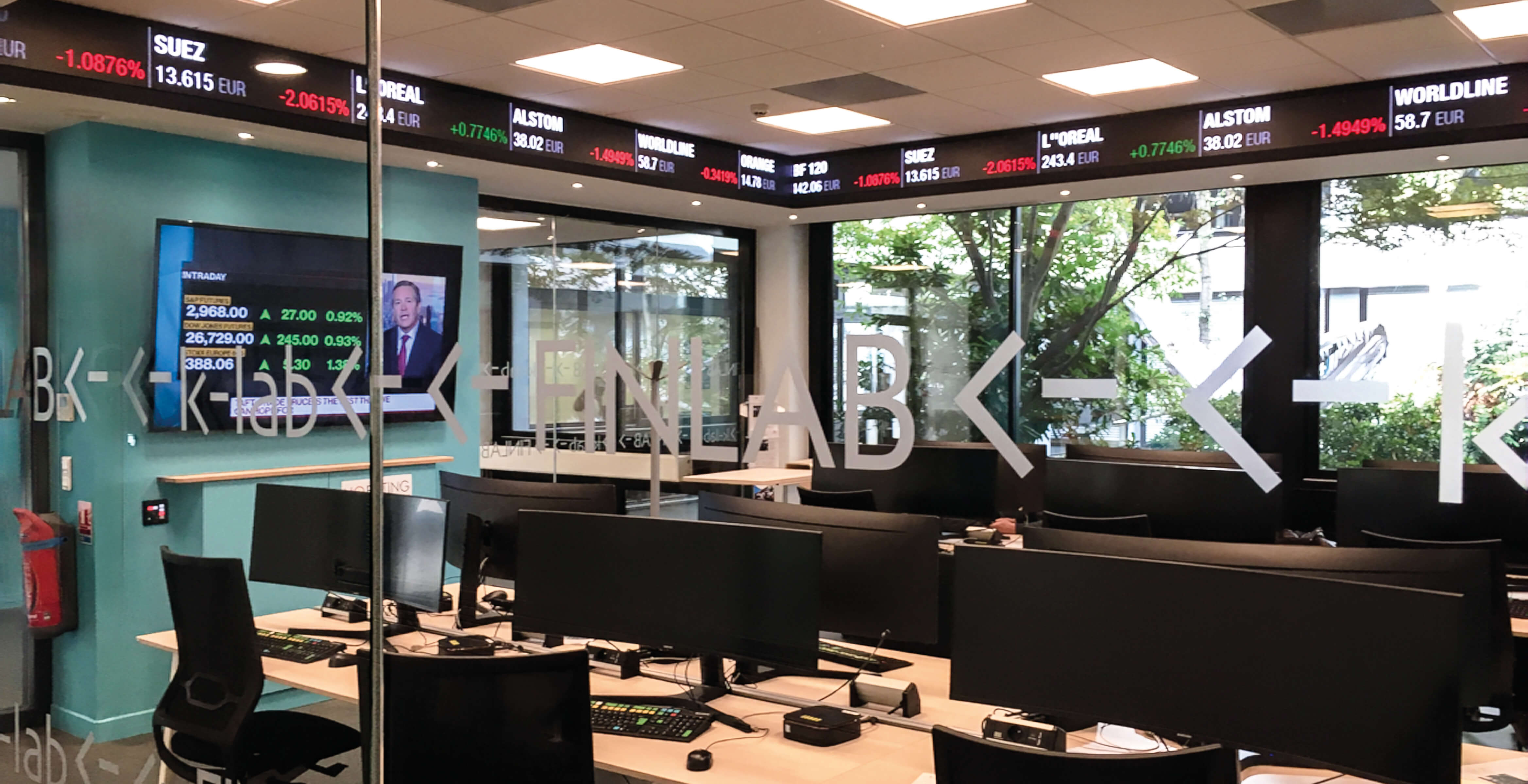 Photo de la salle des marchés du K-Lab de l’Essec avec ordinateurs, écran, défilé du cours des actions.