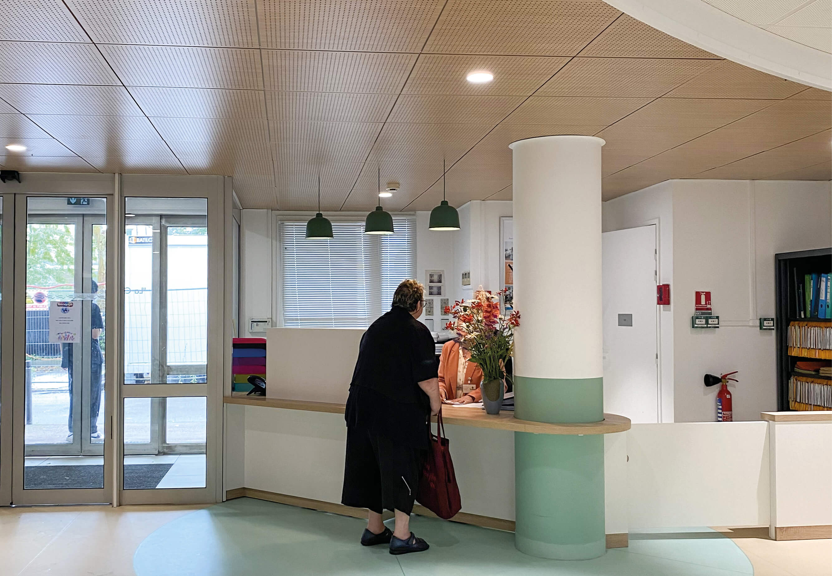 Photo d’une femme s’adressant à l’employé derrière la banque d’accueil après le réaménagement des espaces communs de l’Ehpad La Citadine de Massy