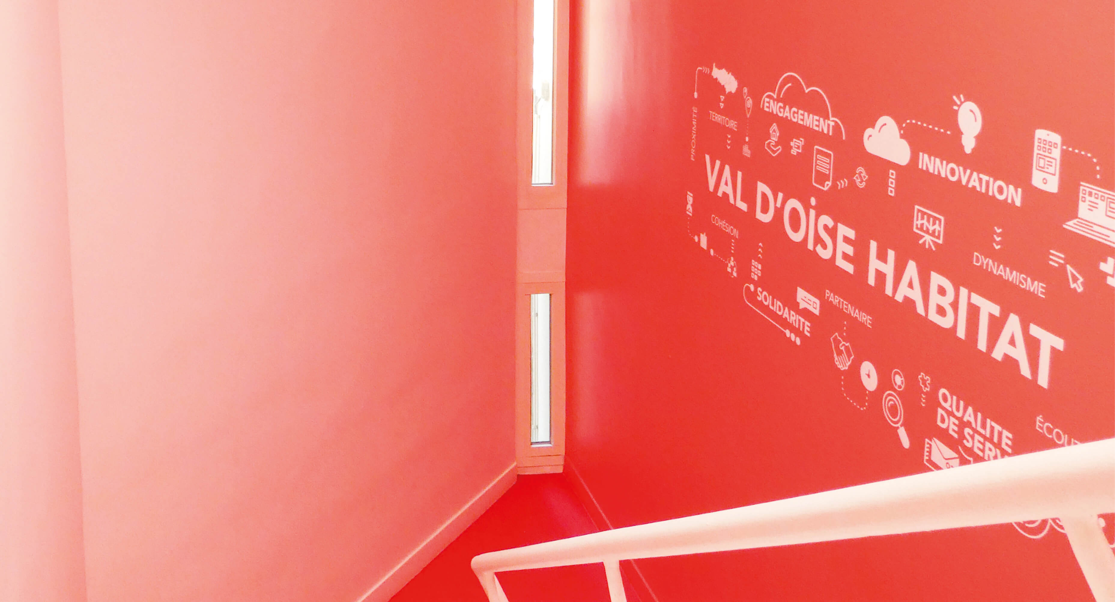 Photo montrant le logo de Val d’Oise Habitat sur fond rouge avec des mots marquant l’engagement de l’établissement après le réaménagement du siège social La Palette.