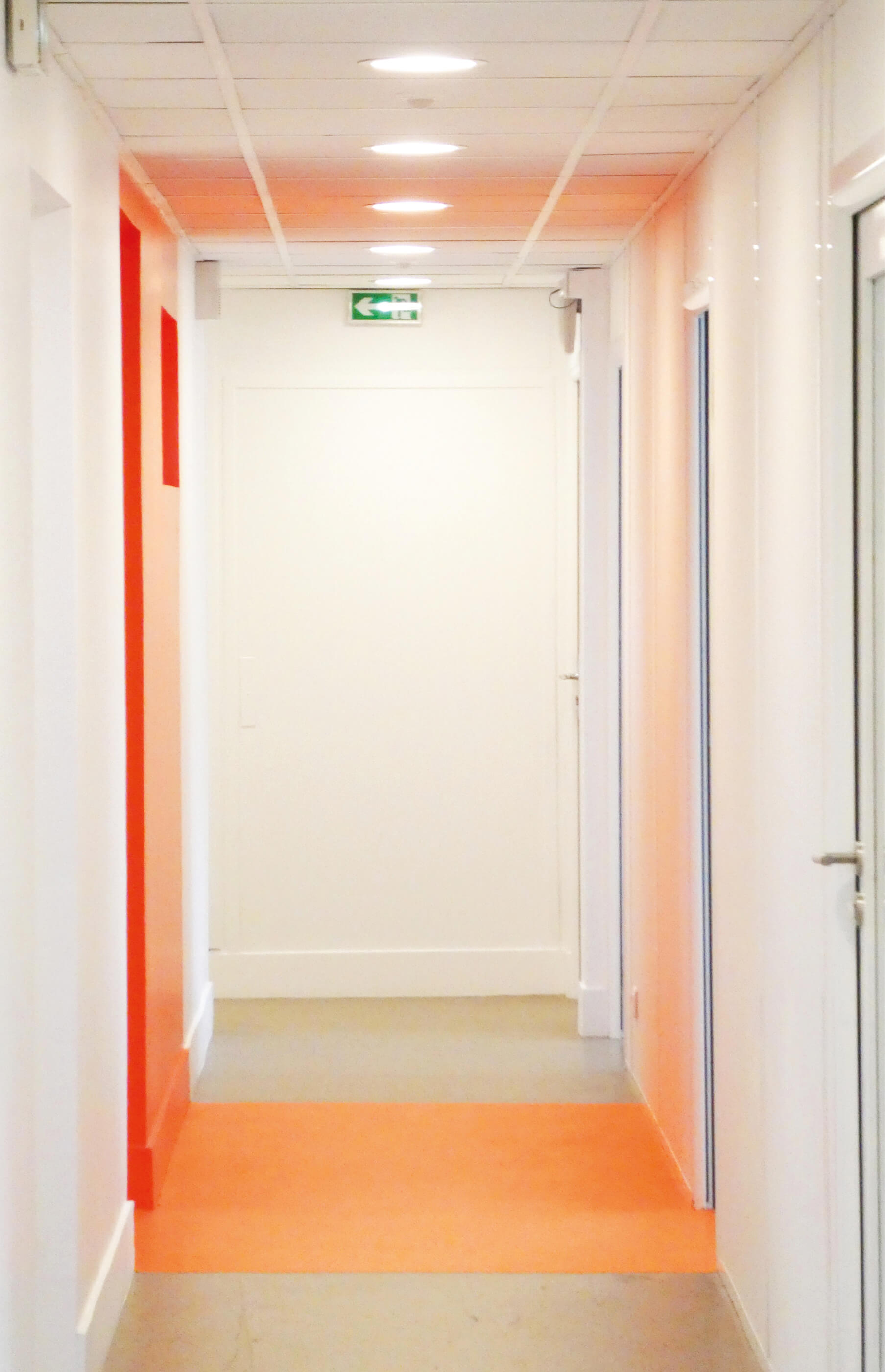Photo d’un couloir aux murs blancs avec une partie peinte en rouge et, au sol, en orange, le réaménagement du siège de Val d’Oise Habitat La Palette.
