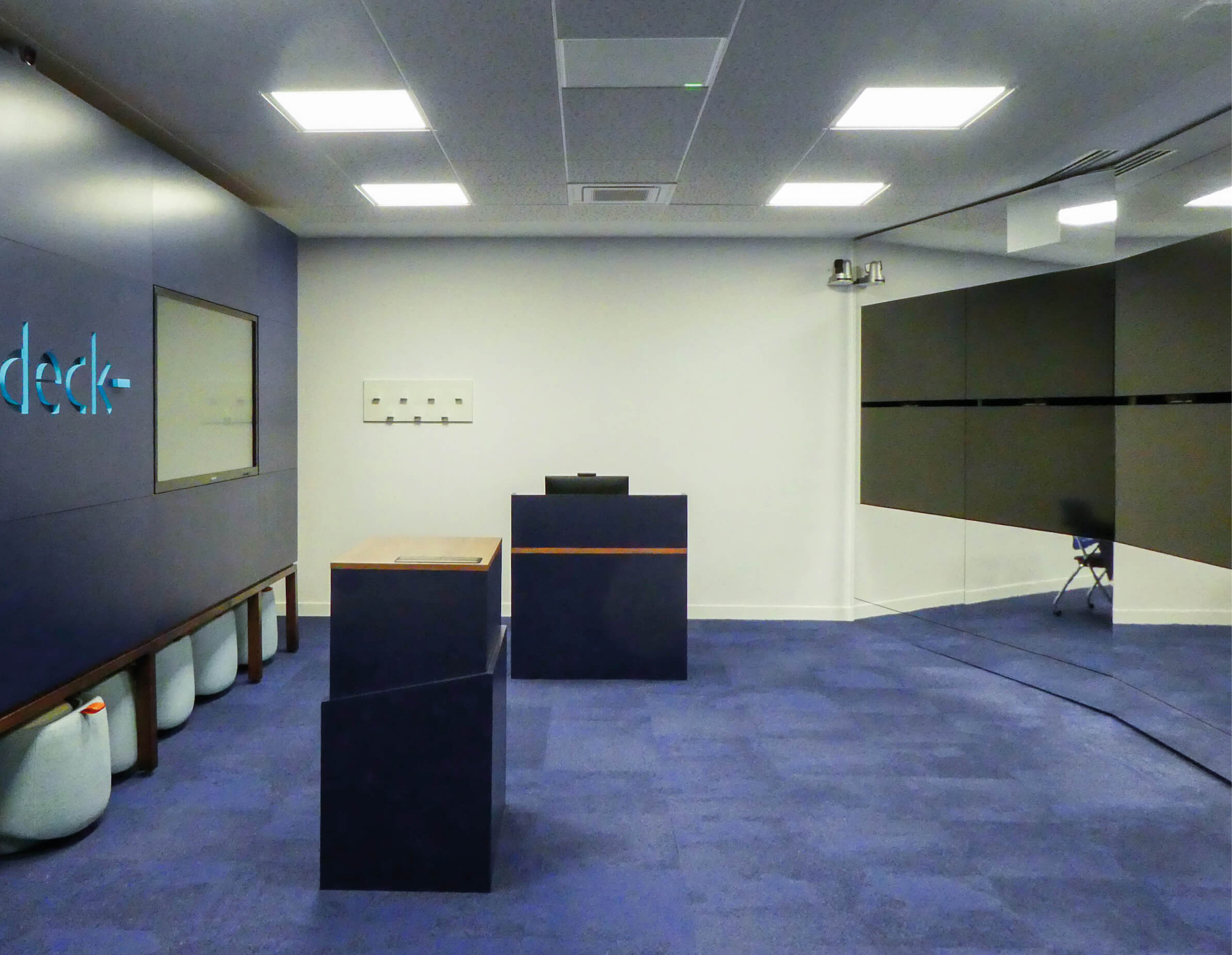Photo de la salle virtuelle de l’Essec, le Deck, finie avec les sièges rangés dans leur niche, les pupitres et le mur d’écrans intégrés à des surfaces miroir.