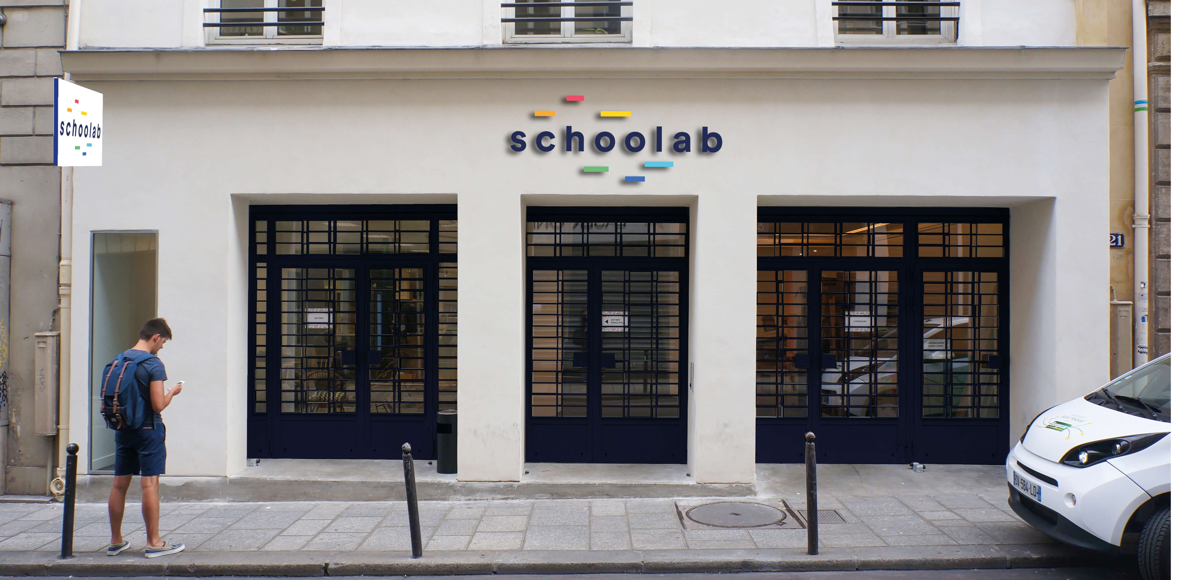Photo de l’entrée du Schoolab depuis la rue avec un homme qui patiente devant.