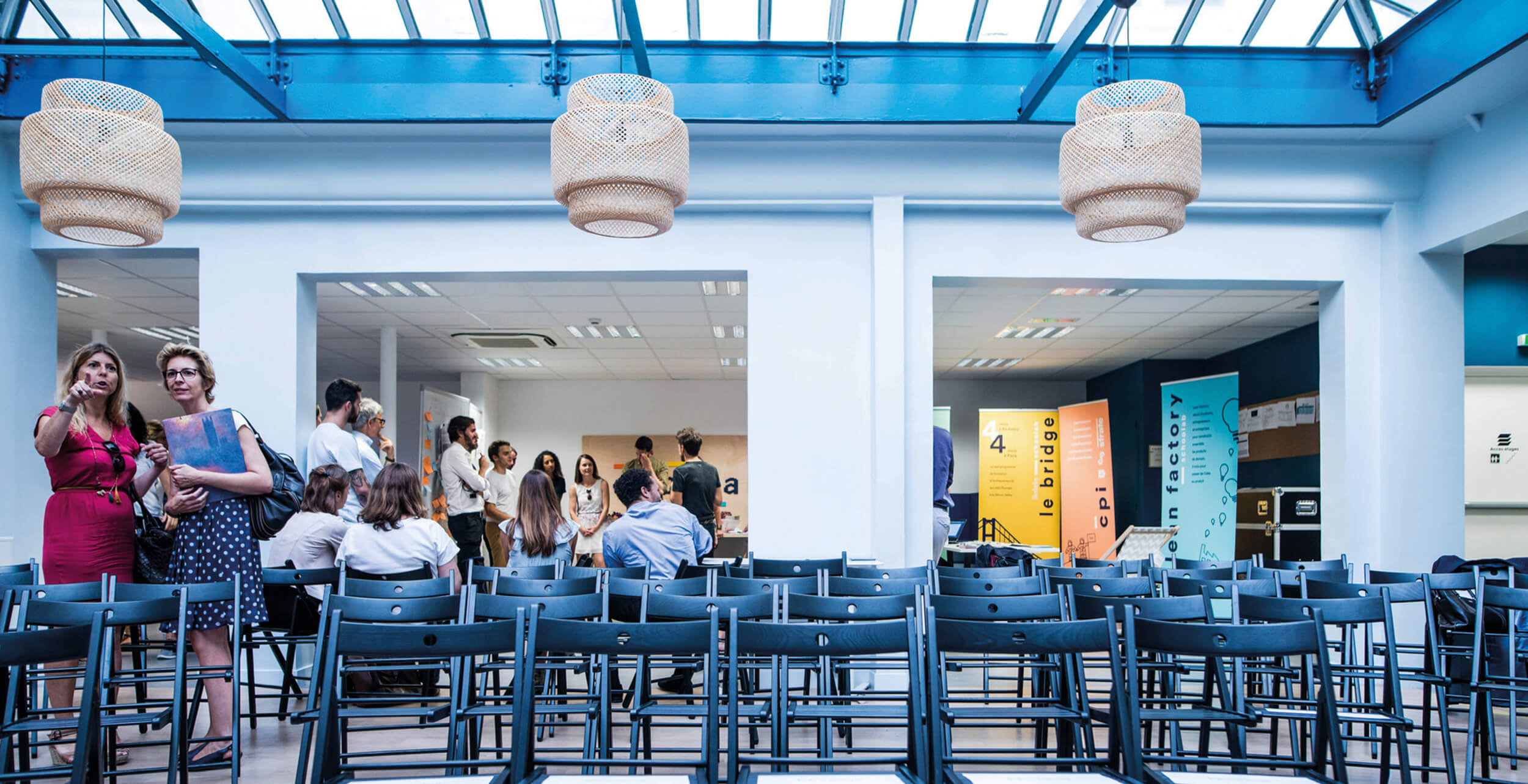 Photo d’un évènement après l’aménagement du Schoolab avec des chaises disposées sous la verrière et de nombreuses personnes qui discutent.