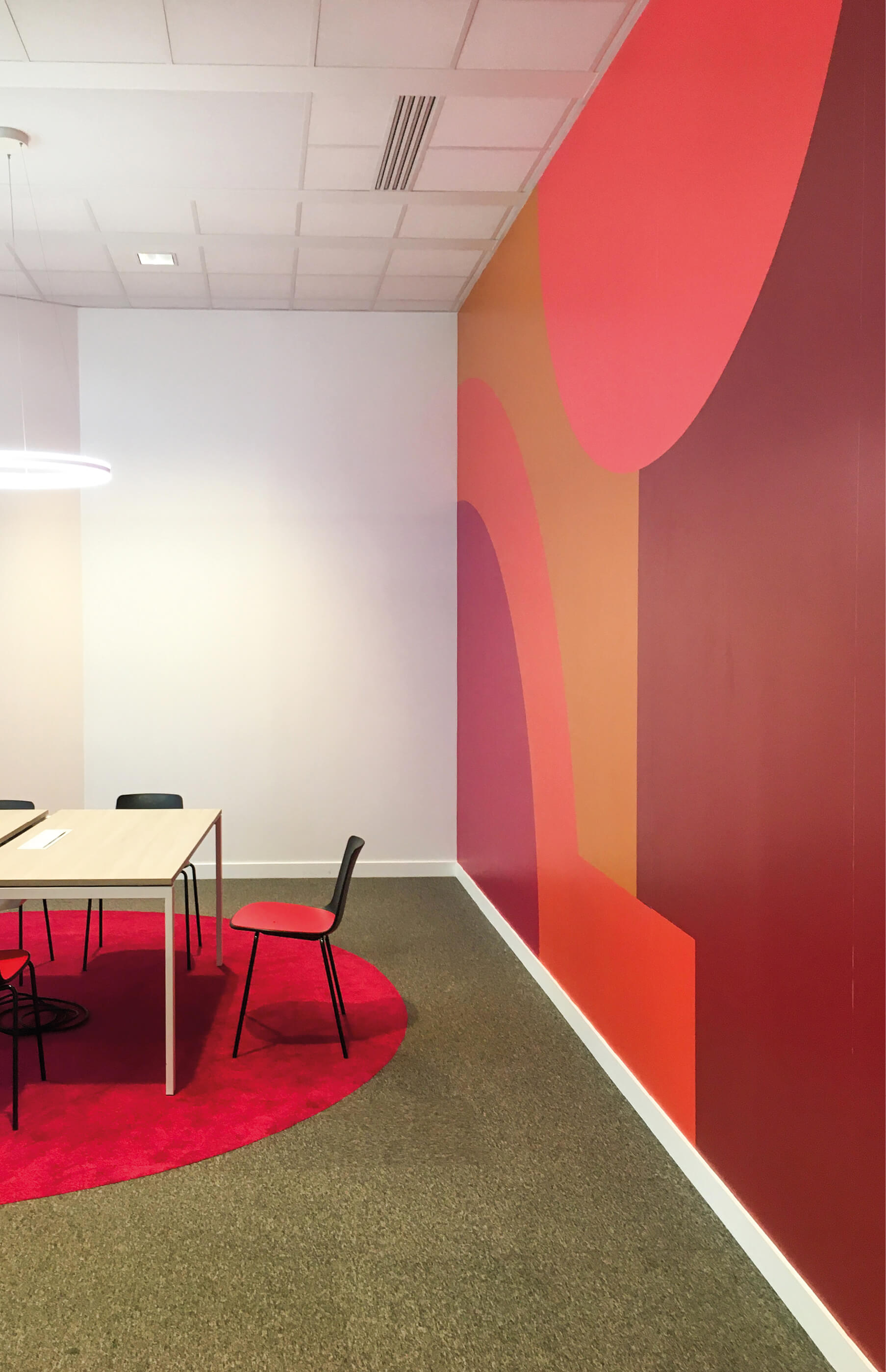 photo d’une table dans une salle de réunion dont le mur est rehaussé d’une fresque dans les tons rouges après le réaménagement du siège social de la société Iqera
