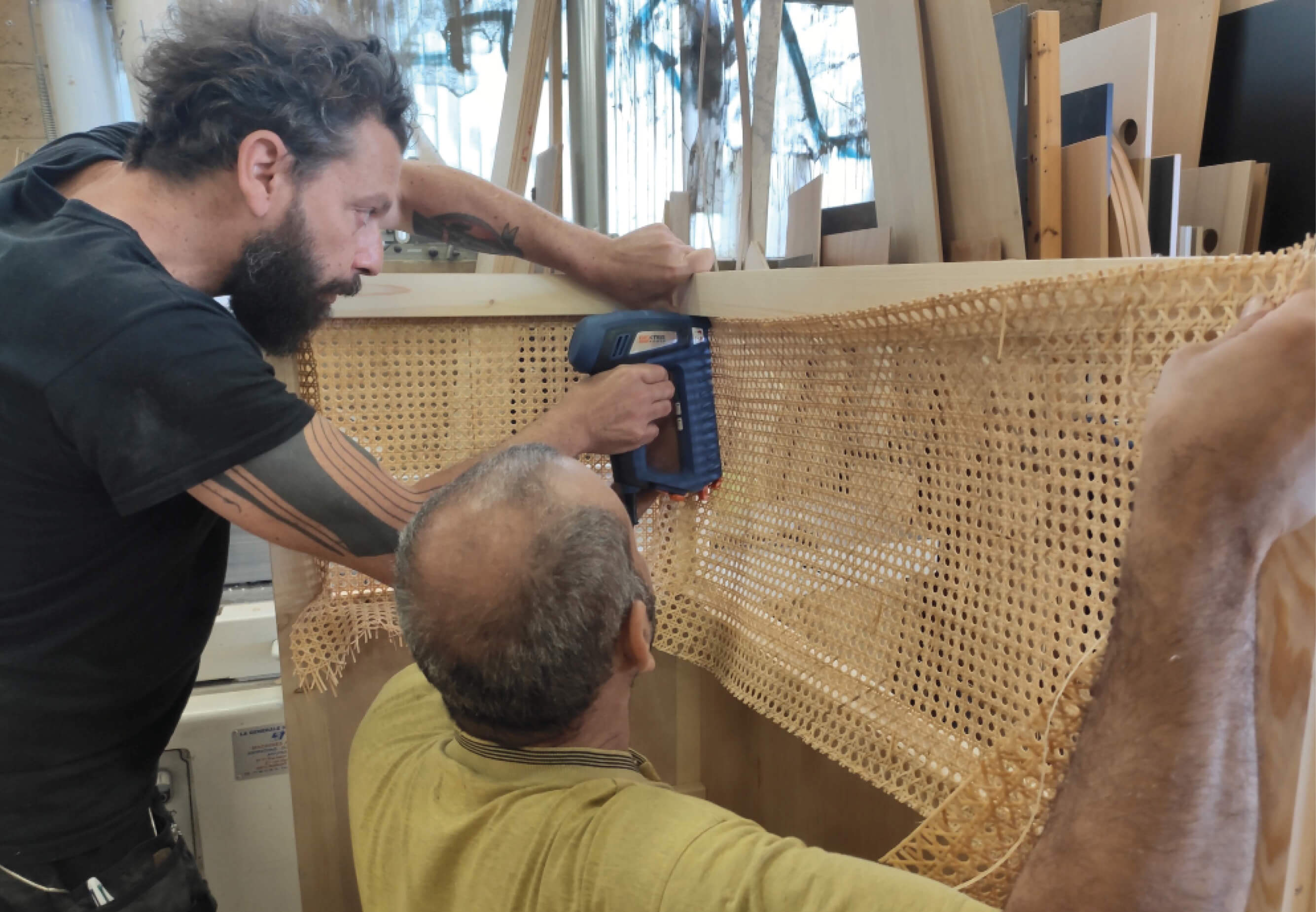 Photo de deux hommes fixant un cannage en rotin sur une structure destinée à habiller la banquette de l’espace échanges après réaménagement du siège social de la société Iqera