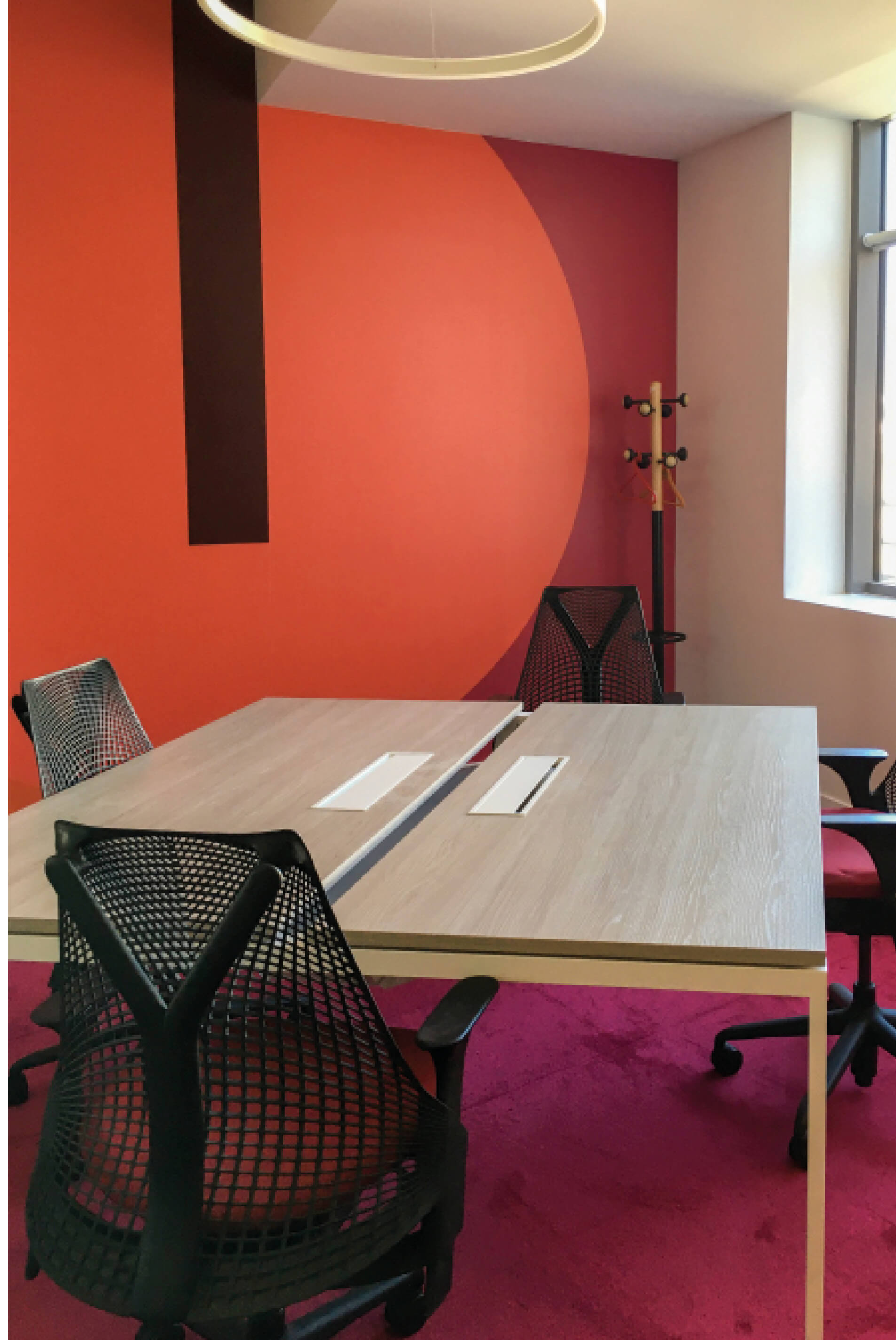 Photo d’une table en salle de réunion mariant un tapis rose à une fresque murale dans des tons chauds