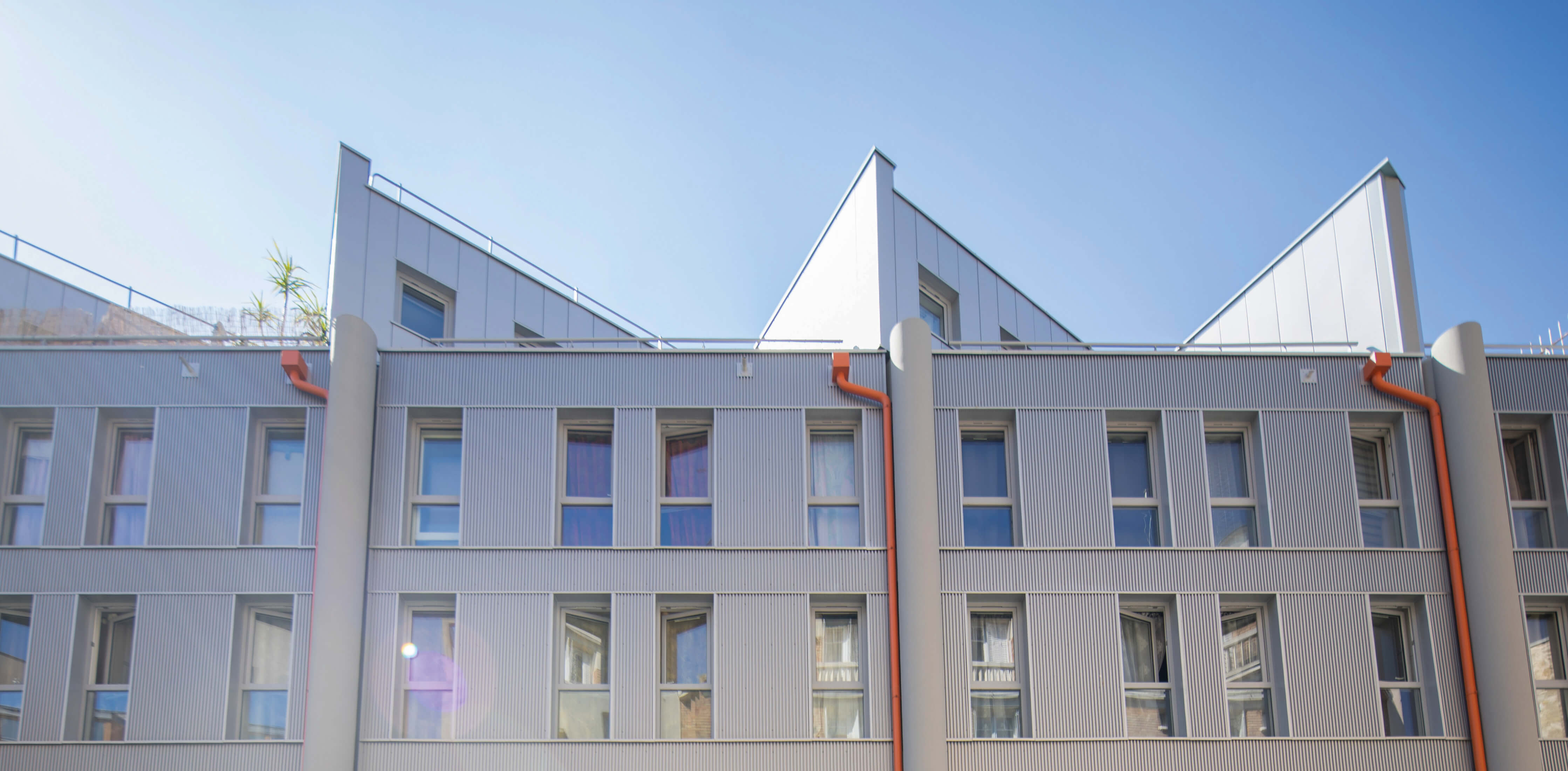 Photo en contre-plongée, avec ciel bleu en fond, de la façade de l’immeuble de la rue de Fontarabie après réhabilitation énergétique plan climat