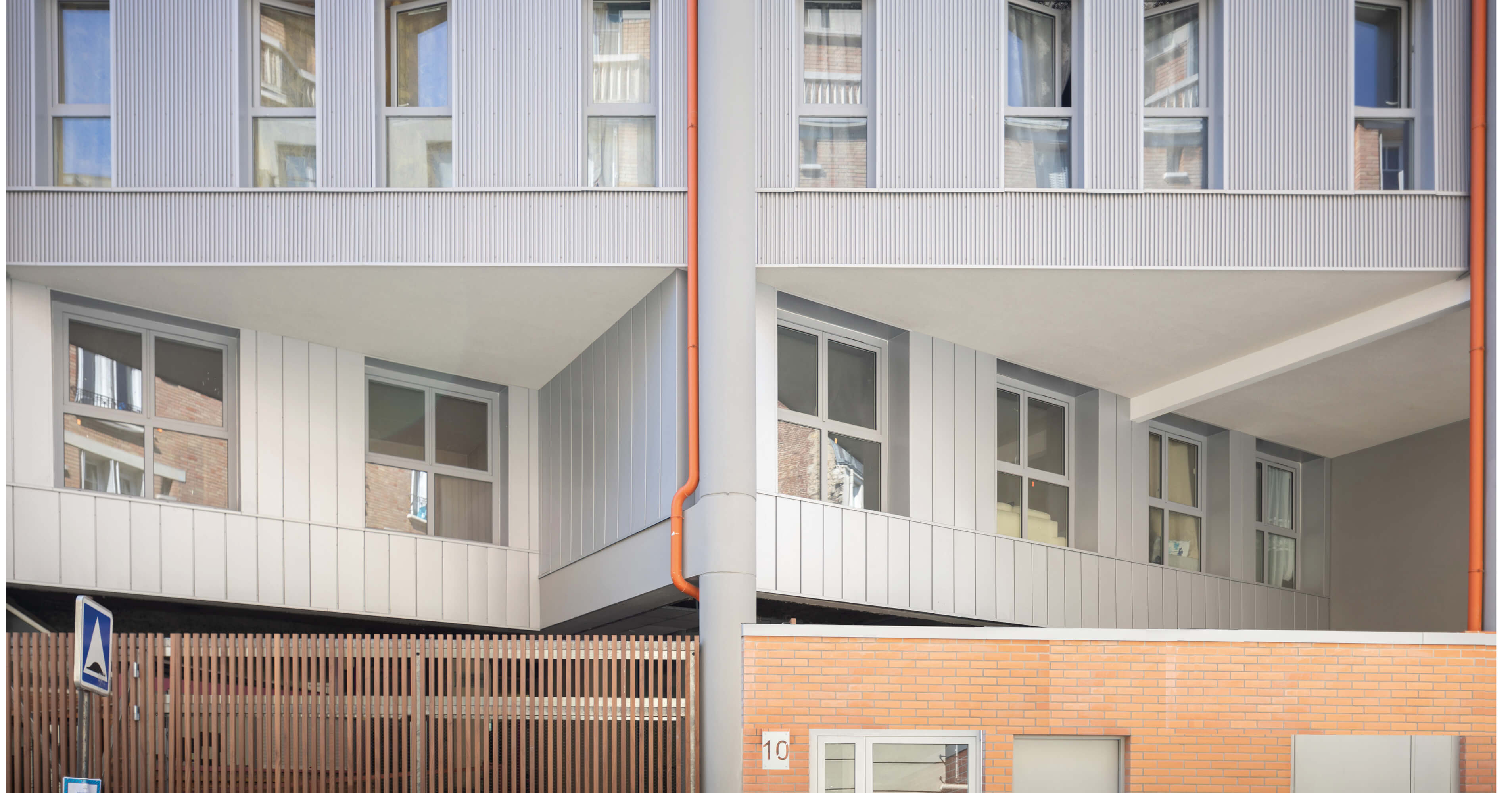 Photo des fenêtres la façade acier de l’immeuble de la rue de Fontarabie avec tuyaux d’évacuation orange après réhabilitation énergétique plan climat