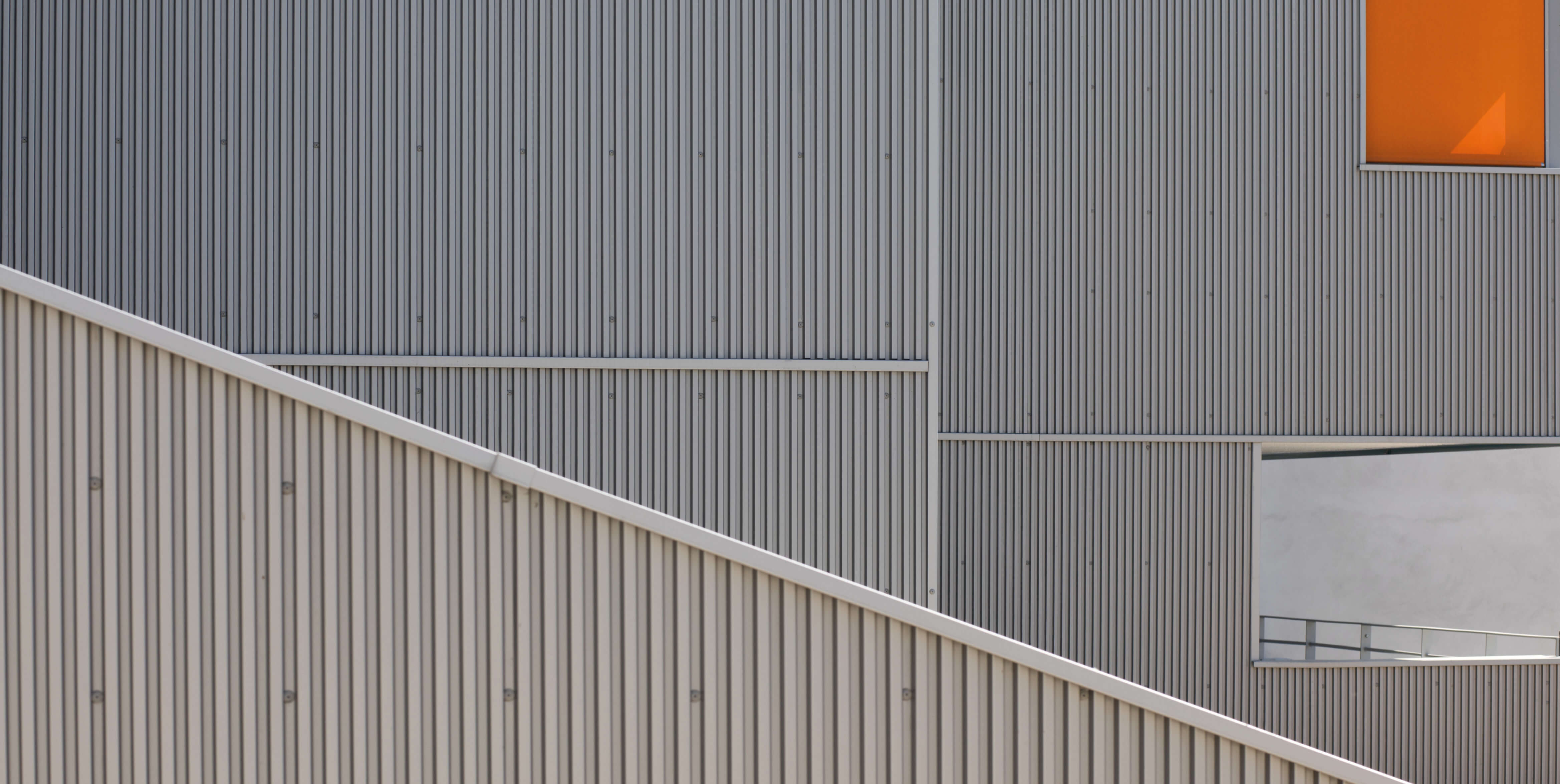 Photo en gros plan des matériaux acier de la façade avec un store orange de la rue de Fontarabie avec l’entrée de l’école avant réhabilitation énergétique plan climat
