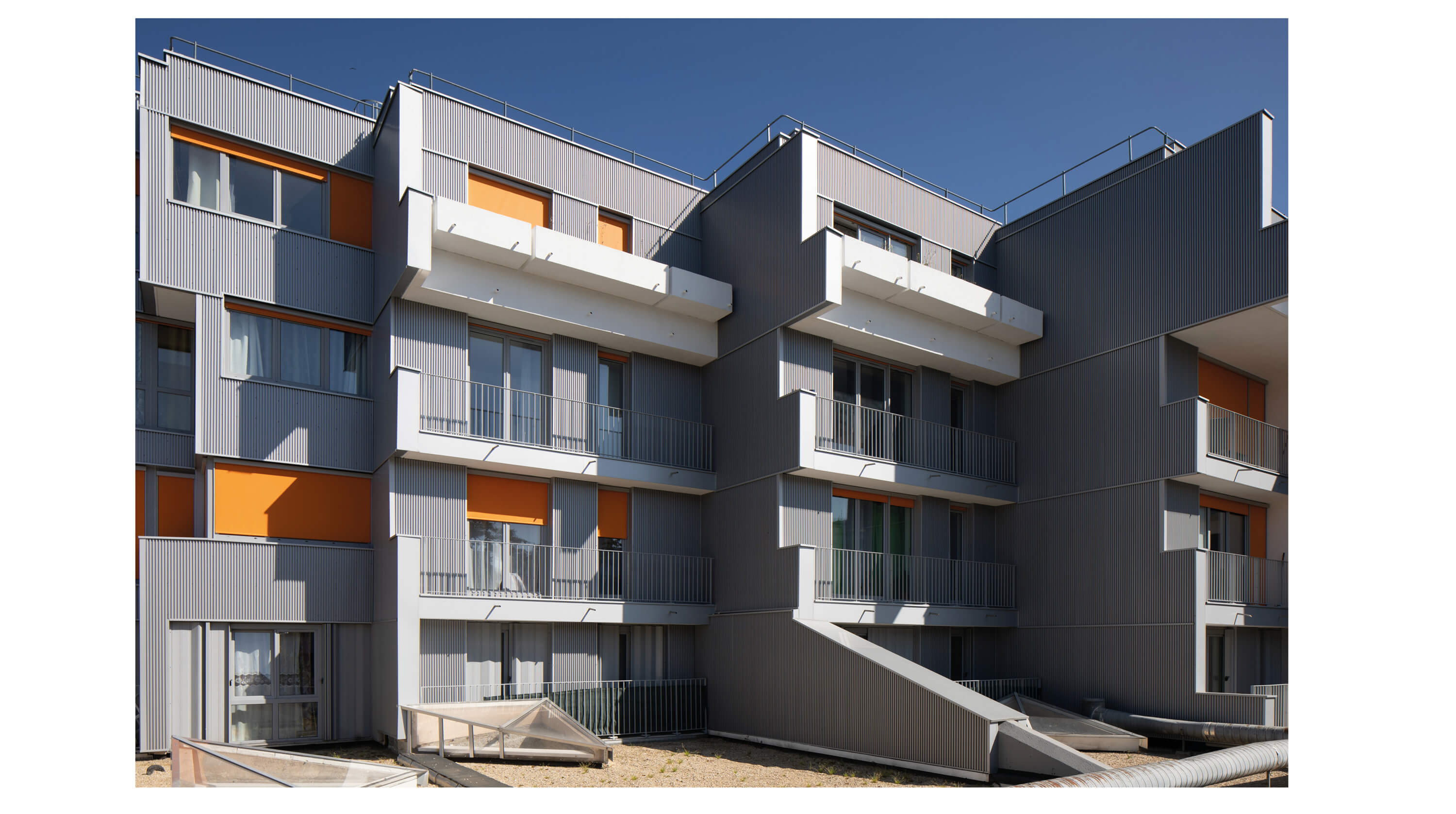 Photo des balcons de l’immeuble rue de la Fontarabie avec façade acier et stores orange après la réhabilitation énergétique plan climat