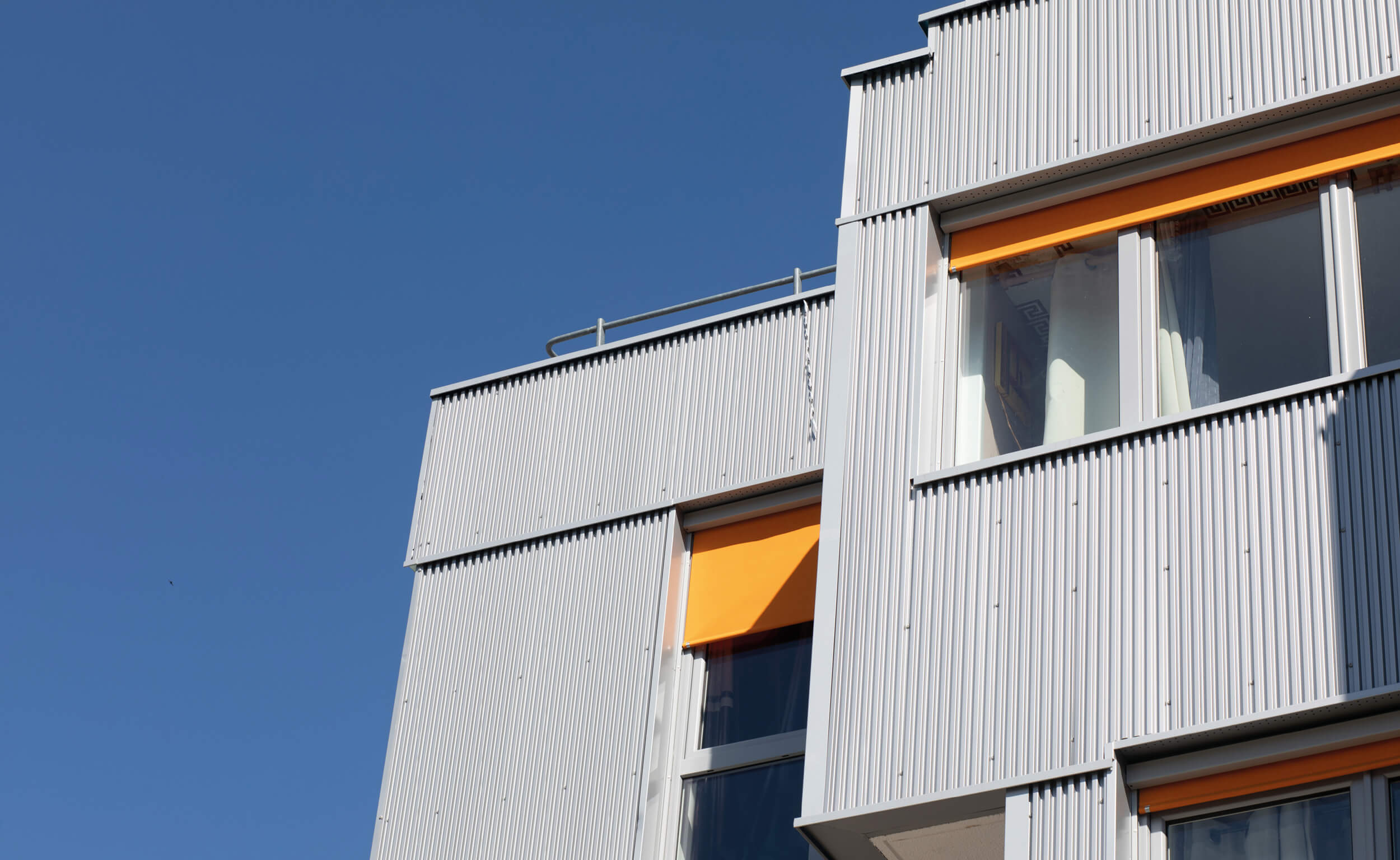 Photo sur fond de ciel bleu du bardage métallique nervuré de la façade rue de Fontarabie après réhabilitation énergétique plan climat