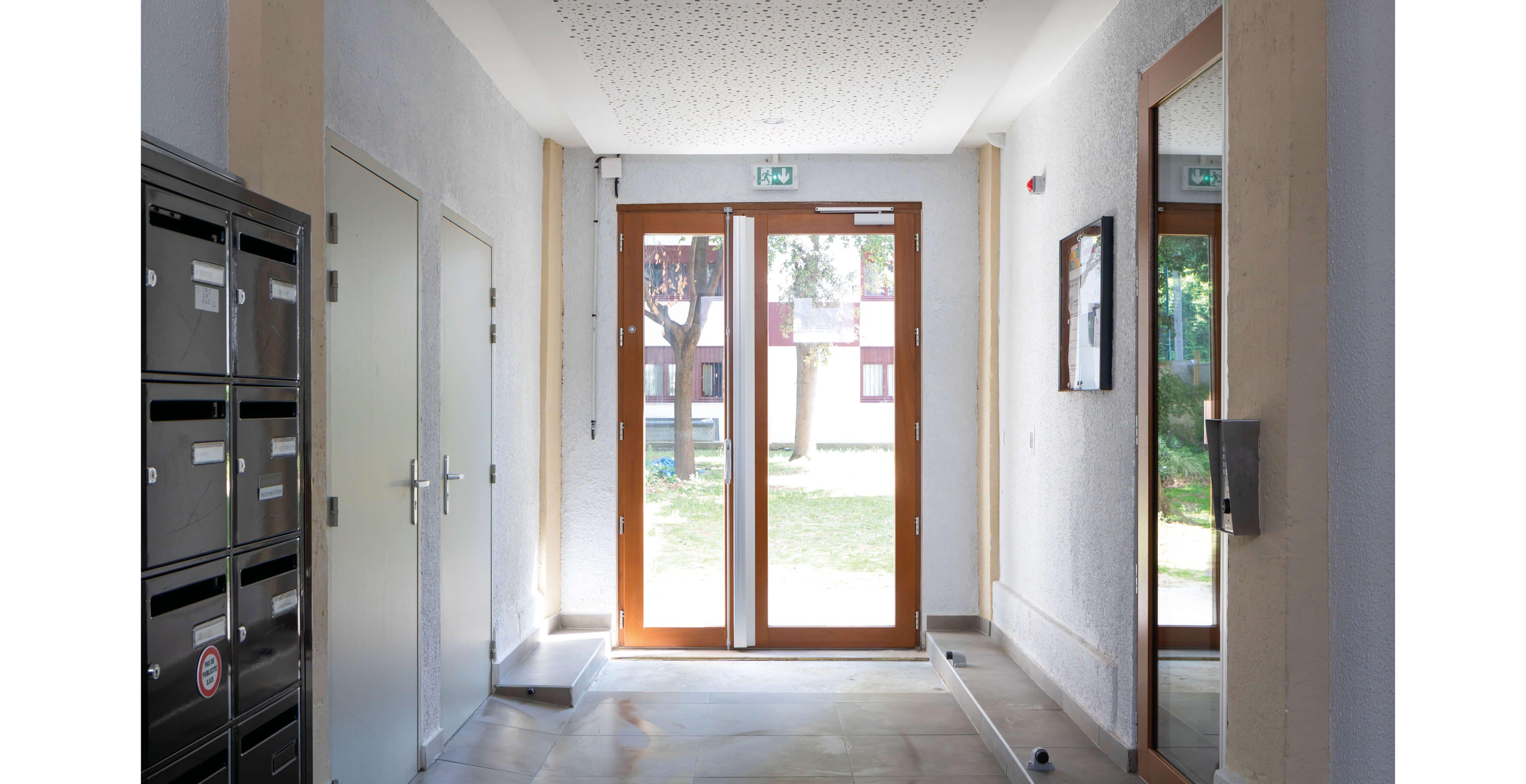 Photo du hall d’entrée montrant les boîtes à lettres et la porte sécurisant l’accès au jardin à l’arrière de l’immeuble du projet réhabilitation plan climat en milieu habité