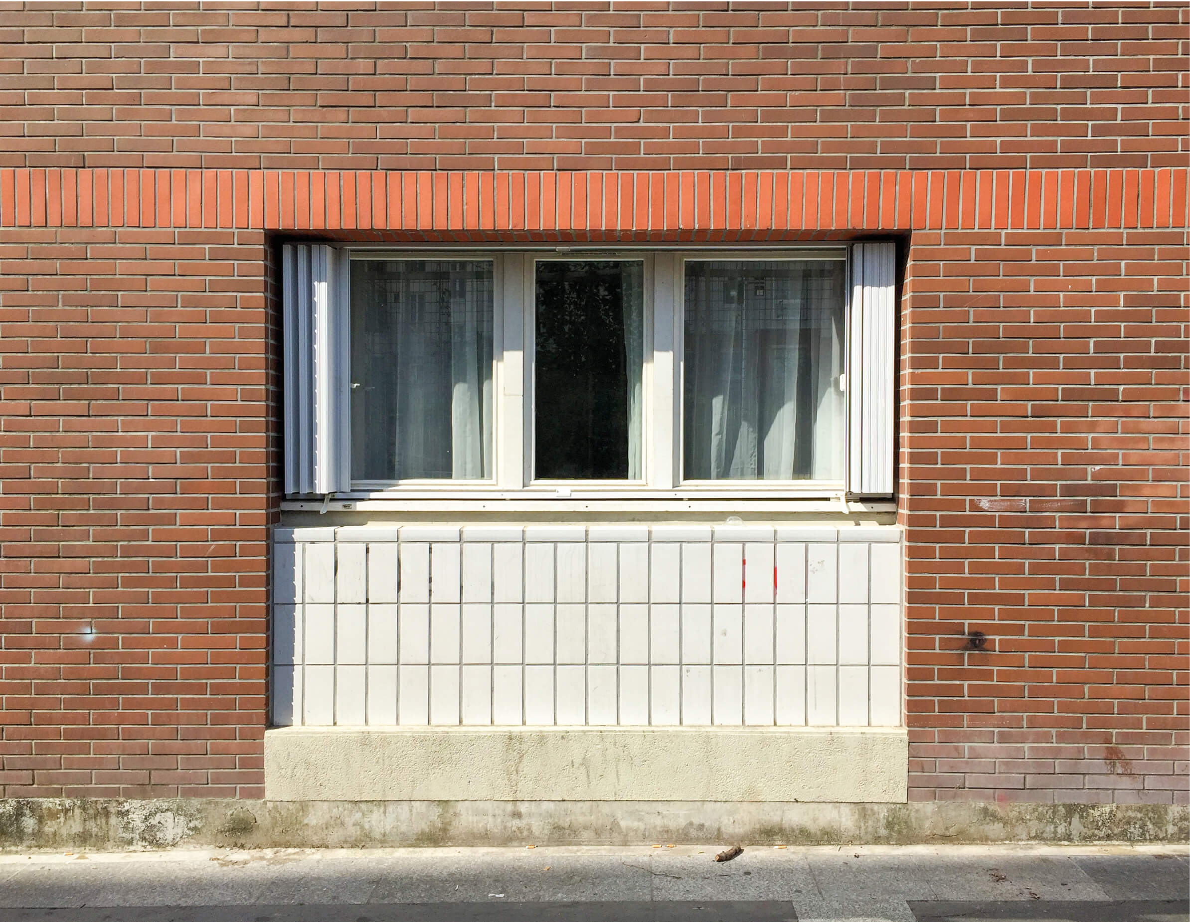 Fenêtre encadrée de briques rouges au rez-de-chaussée du bâtiment concerné par le concours pour la rehabilitation plan climat rue kergomard