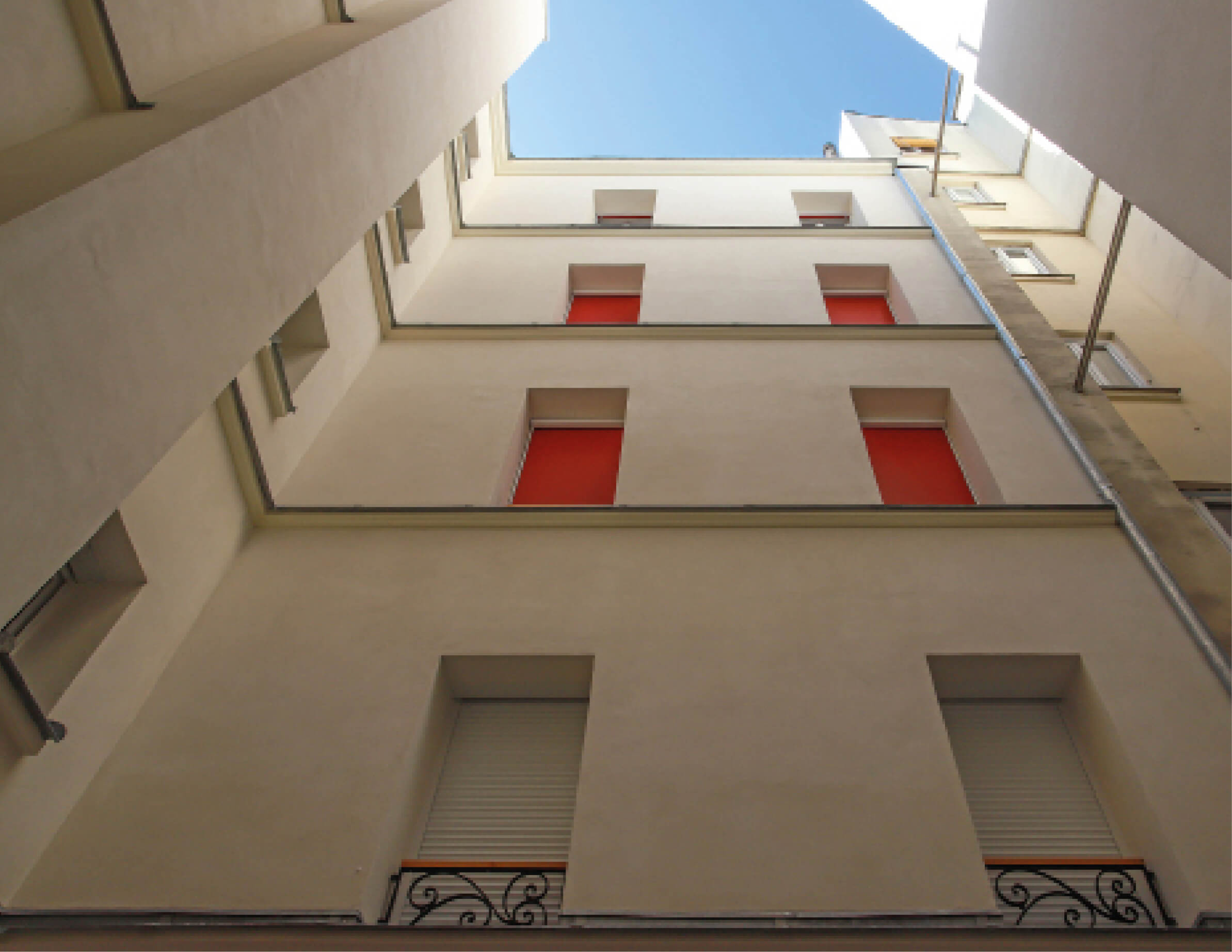 Photo en contre-plongée de façade côté cour avec peinture neuve, occultations rouges et ciel bleu