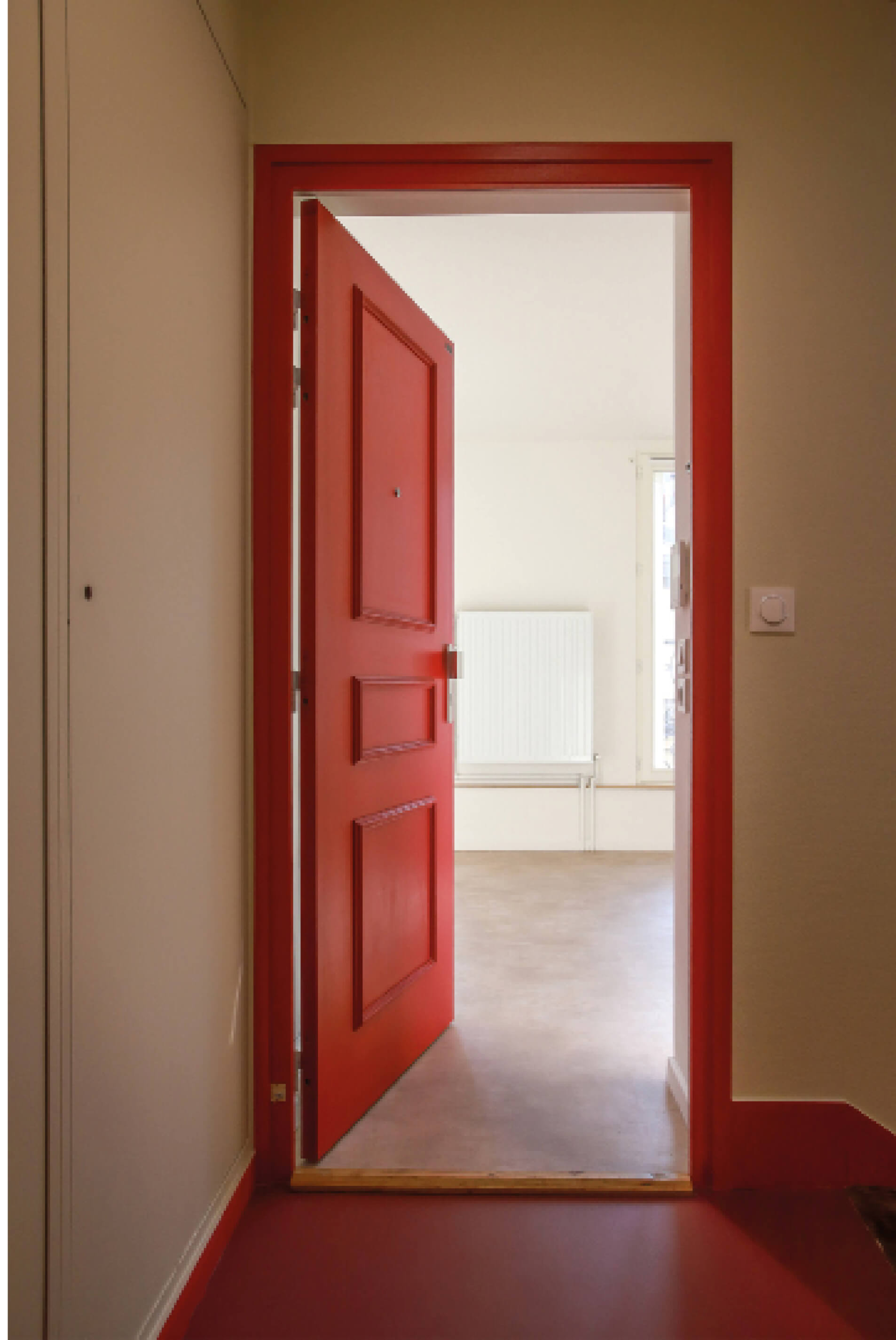Porte d’entrée rouge entrouverte d’un appartement dévoilant les résultats de la restructuration et réhabilitation rue Sauffroy