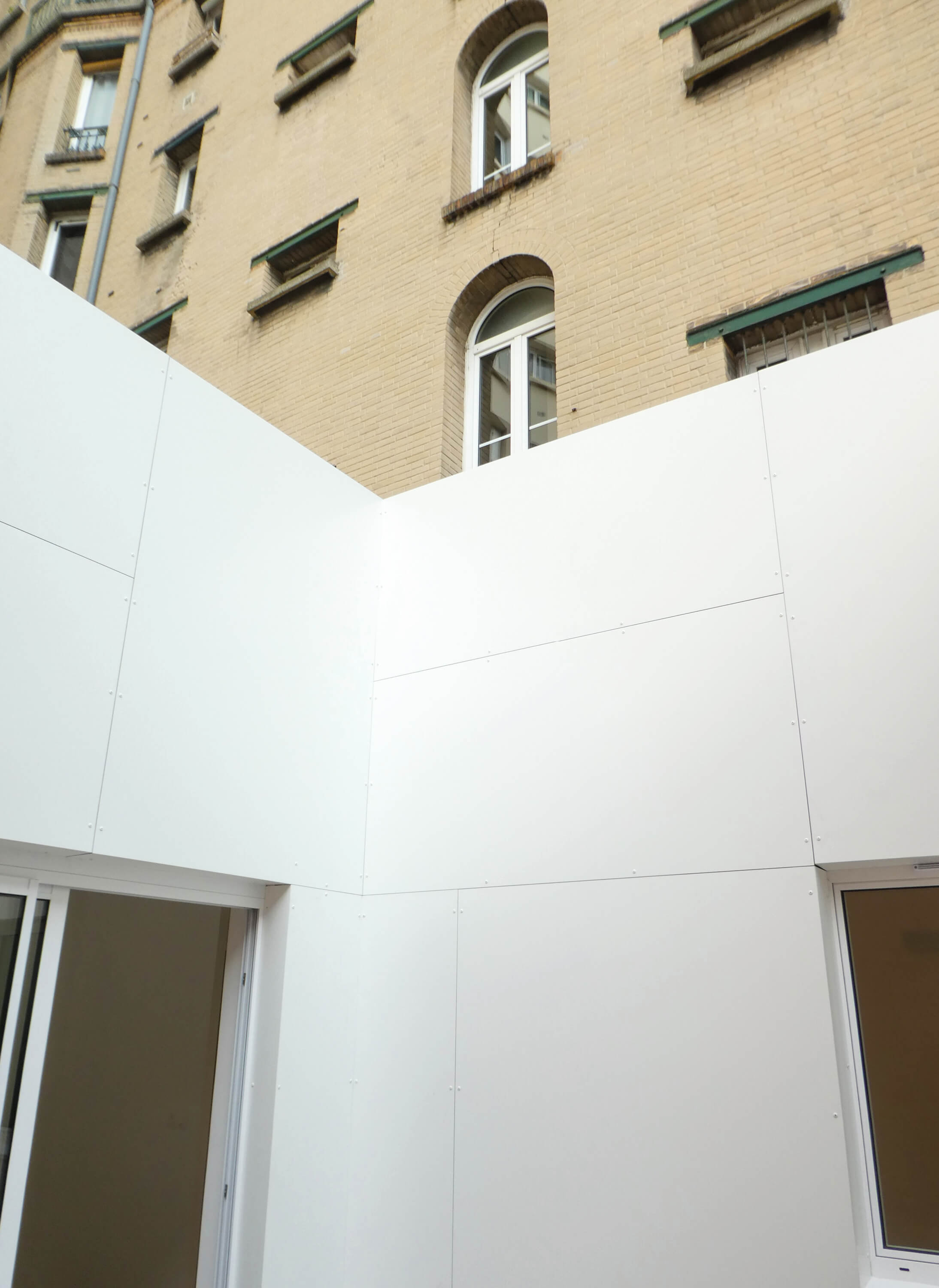 Photo des murs blancs du patio avec immeuble en surplomb après restructuration et reconversion en logement square Eugène Hatton.