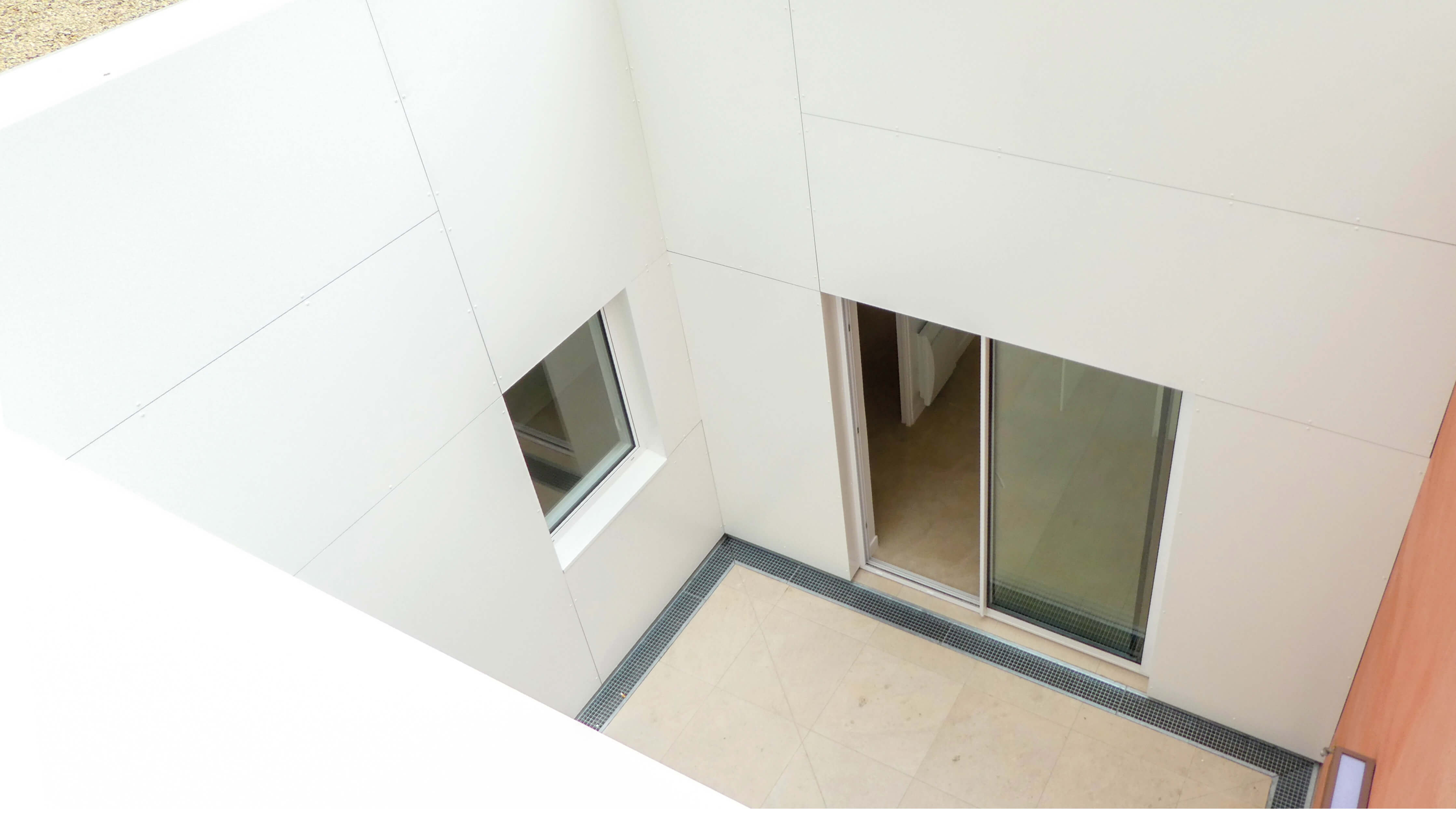 Photo des murs blancs et orangés du patio en contre-plongée et des fenêtres après restructuration et reconversion en logement square Eugène Hatton.