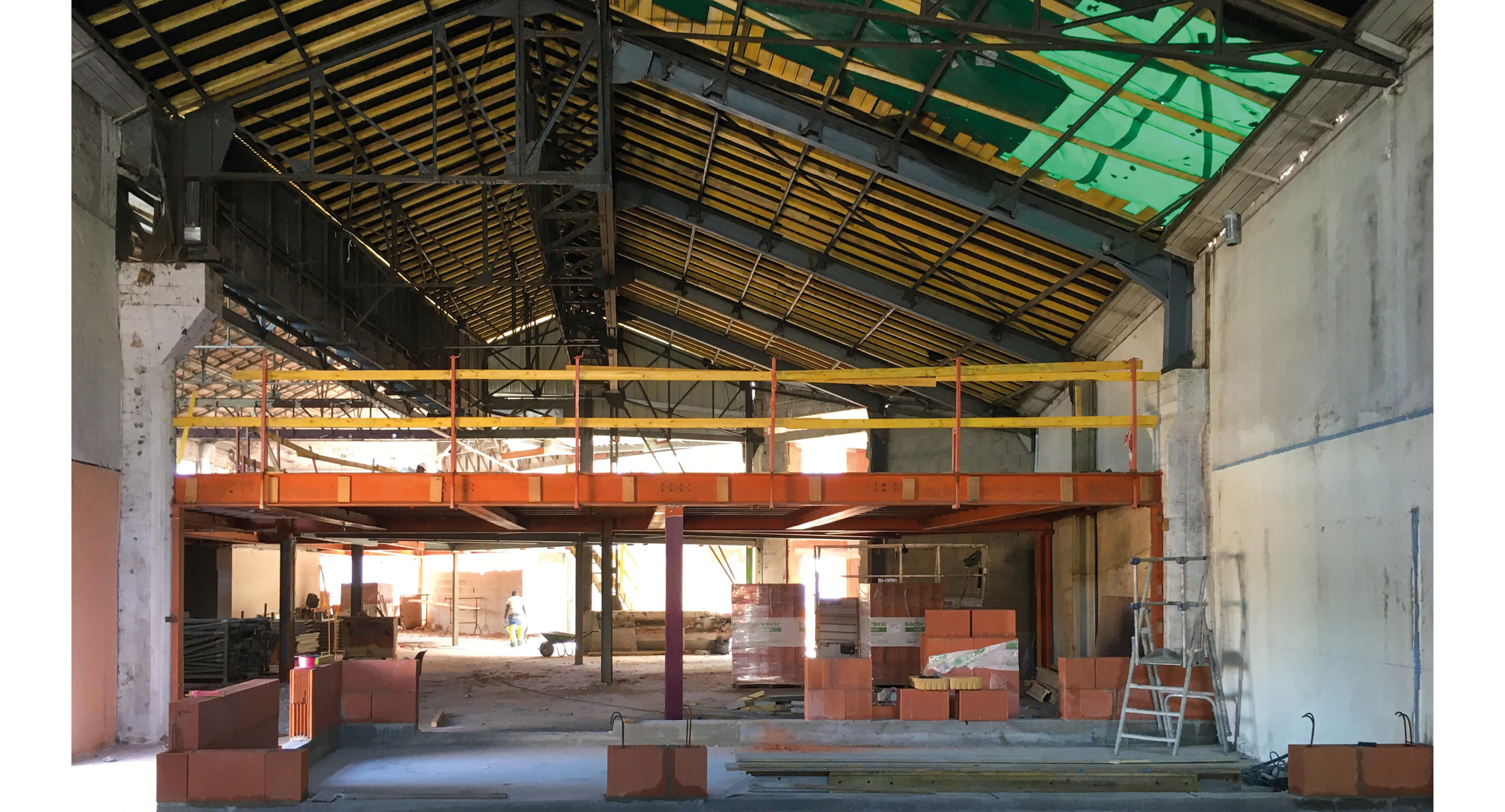 Photo des hangars Timbror avant la reconversion en bureaux avec du materiel de construction, une bache verte sur le toit